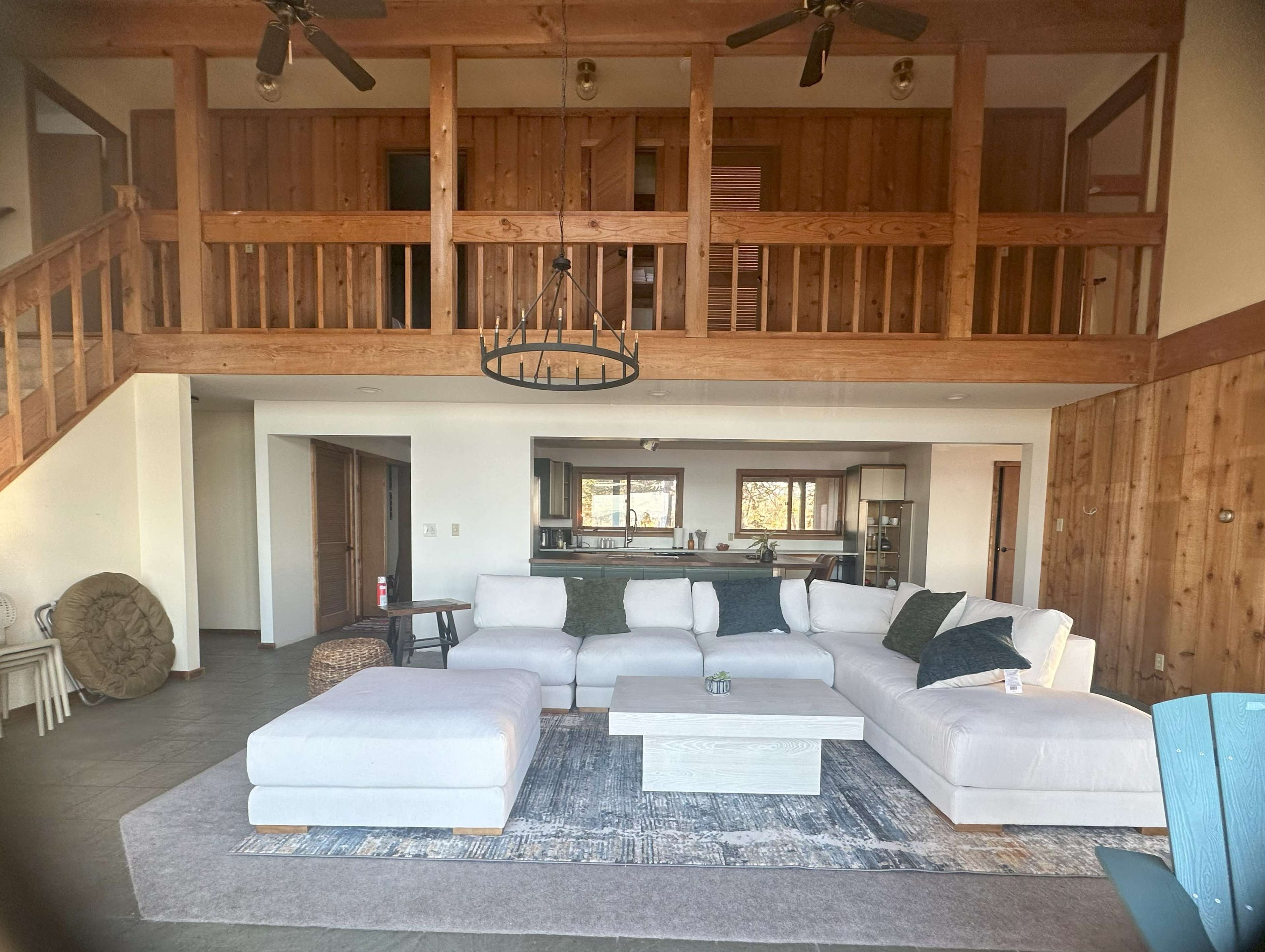 A spacious living room featuring a large sectional sofa, wooden beams, and a kitchen area visible in the background.