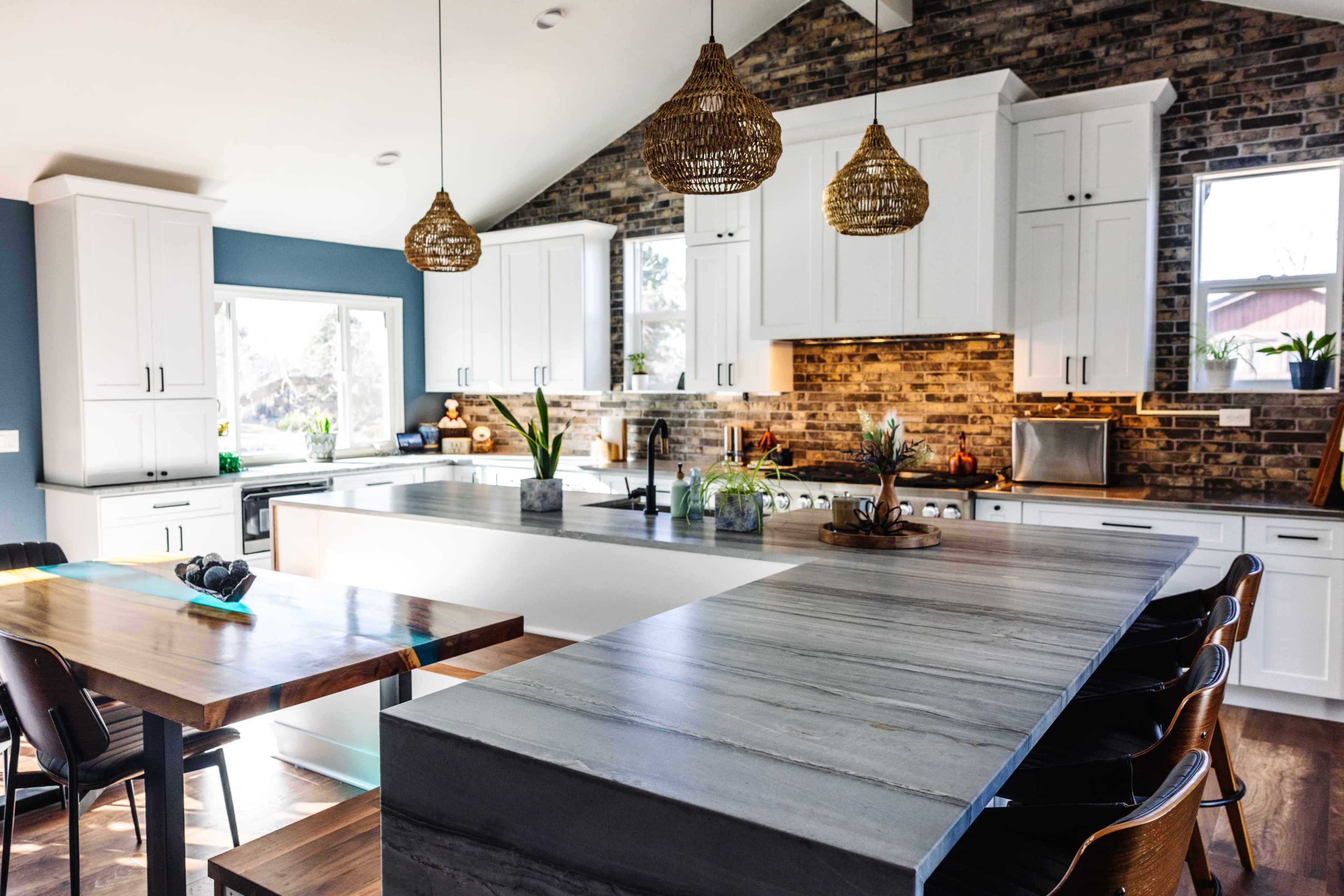 A modern kitchen features white cabinetry, a stone backsplash, and a large island with bar seating, illuminated by woven pendant lights.