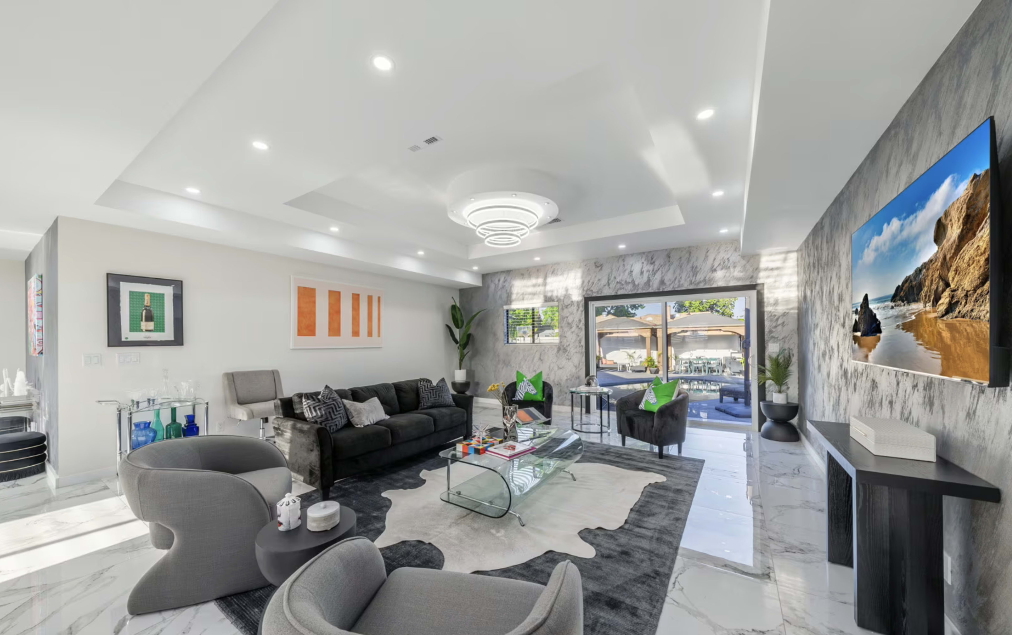 The living room features modern furniture, a glass coffee table, and large windows that open to an outdoor patio.