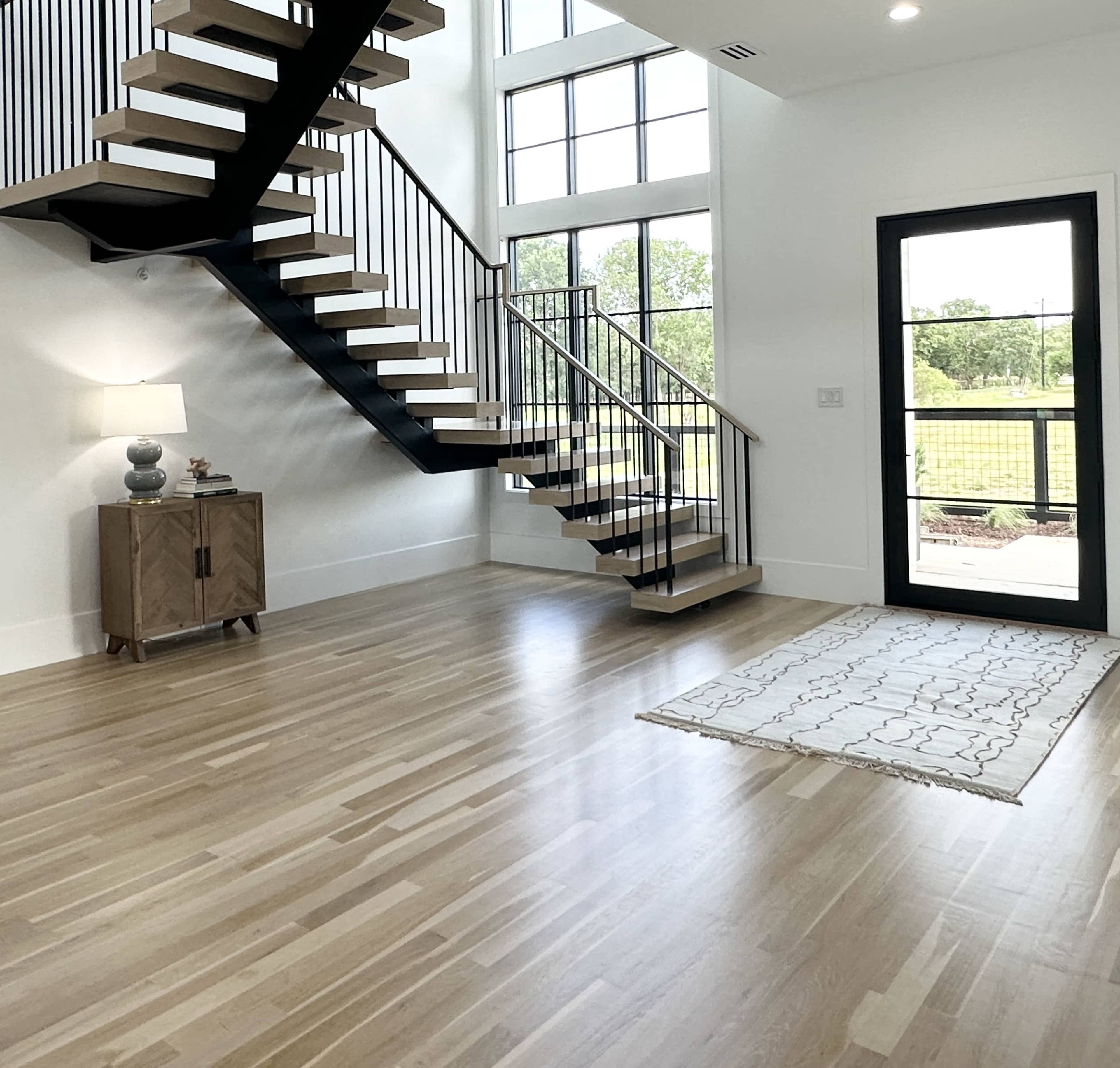 A spacious entryway featuring a staircase with black railings, a wooden cabinet, and a door leading to an outdoor area.