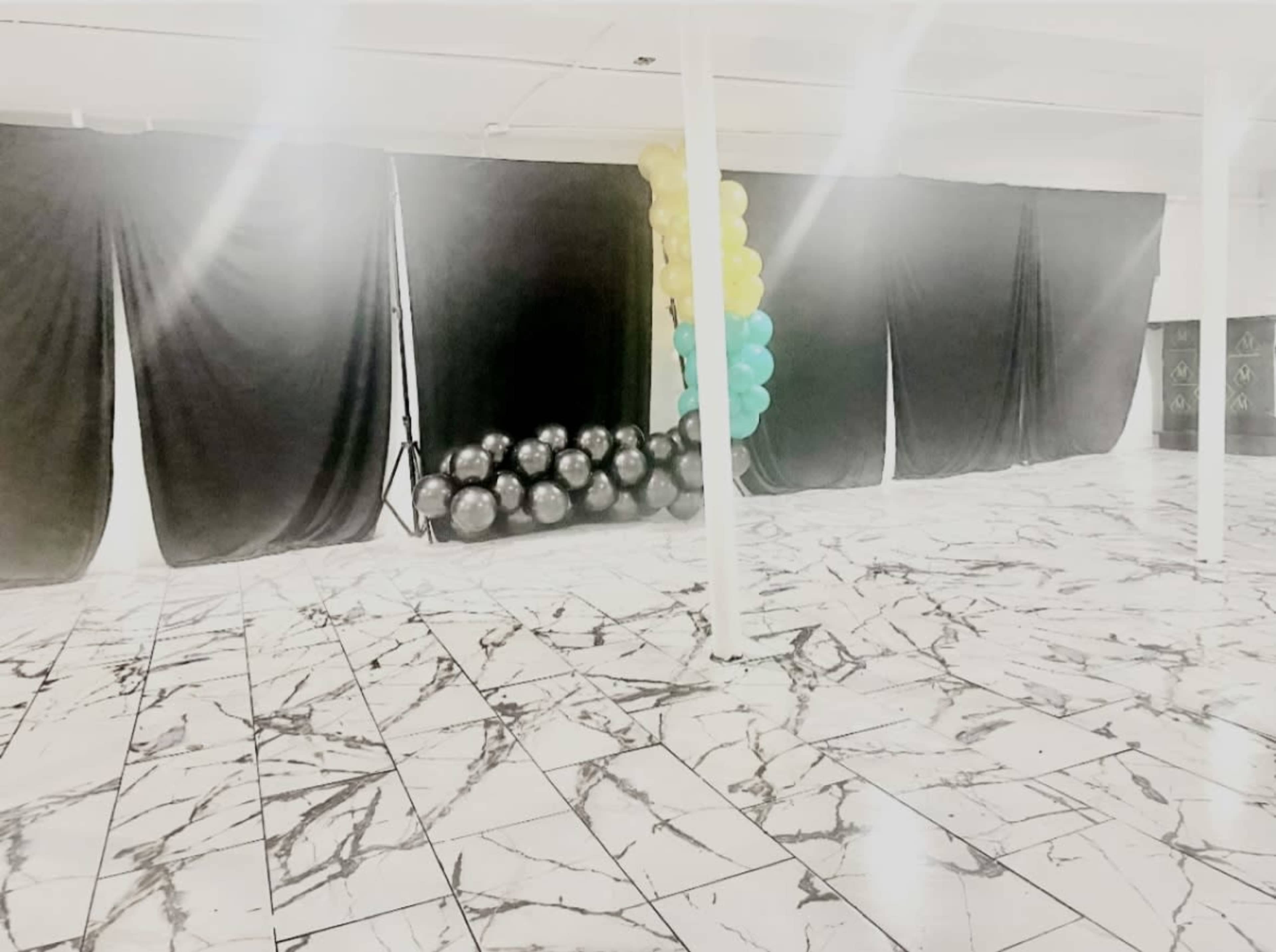 A spacious interior with a marbled floor, black drapes, and a cluster of balloons in teal and yellow on one side.