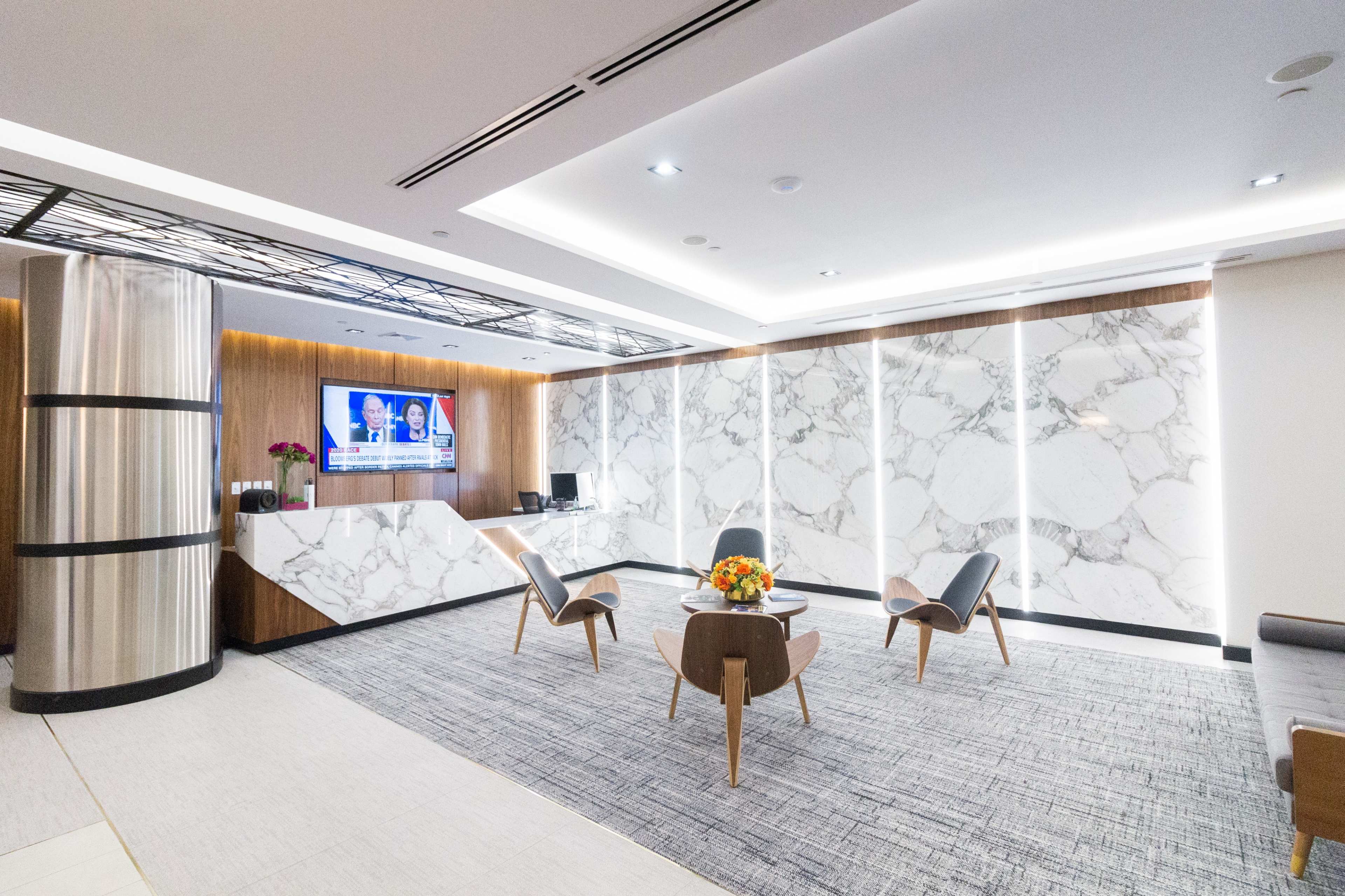 A modern reception area with marble walls, sleek furniture, and a television displaying news updates.