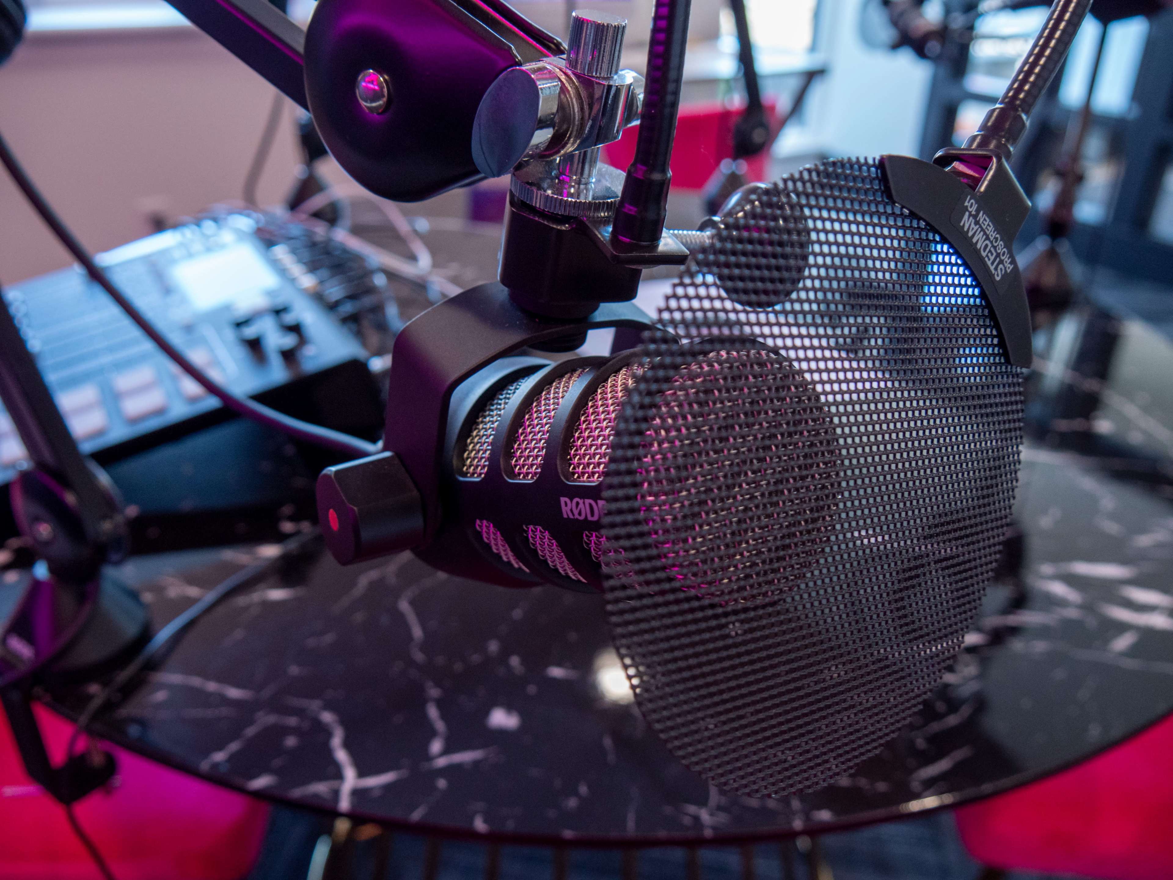 A microphone with a pop filter is positioned on a marble table next to audio equipment in a well-lit room.
