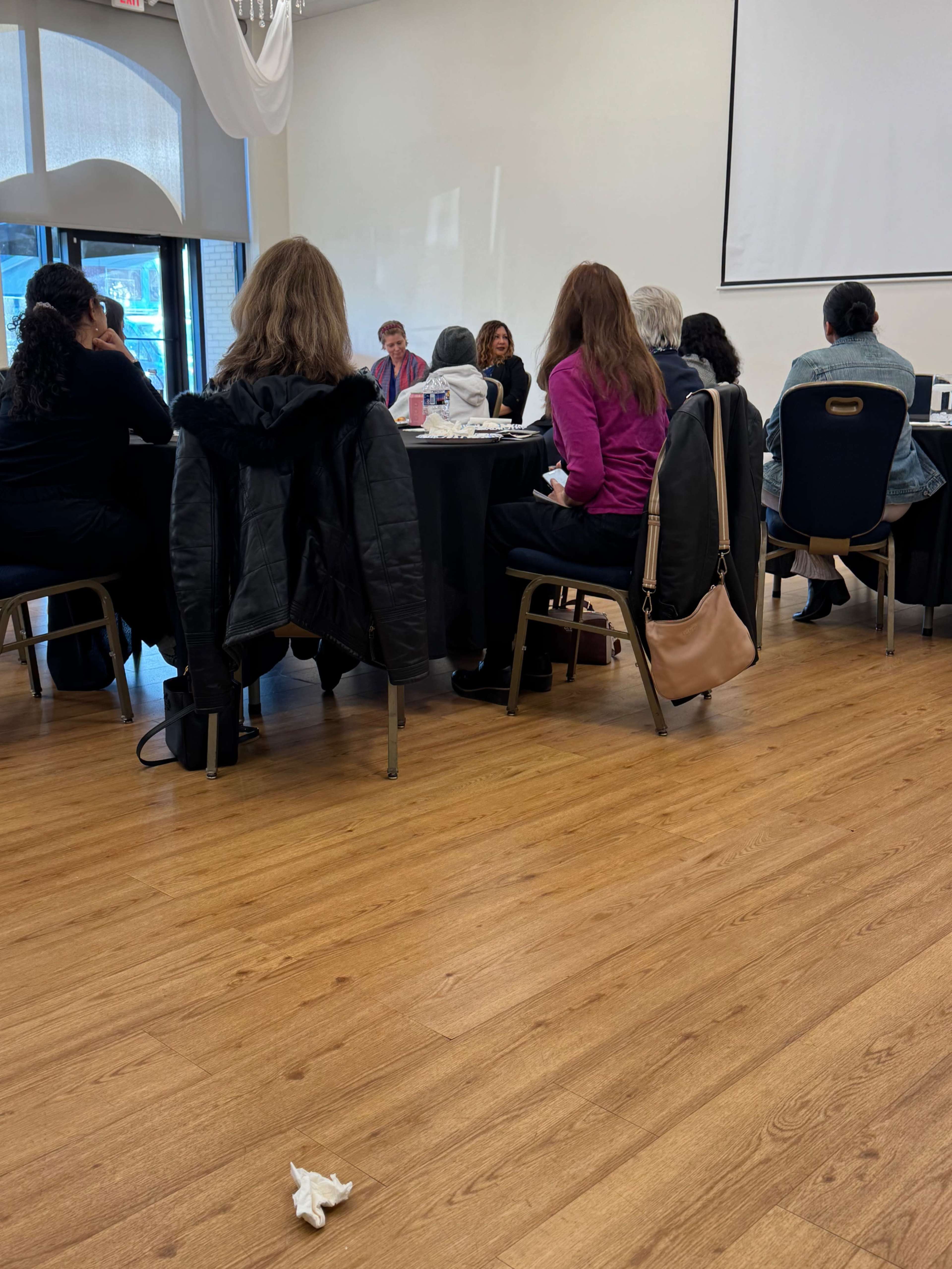 A group of individuals is seated at tables in a conference room, participating in a discussion or presentation.