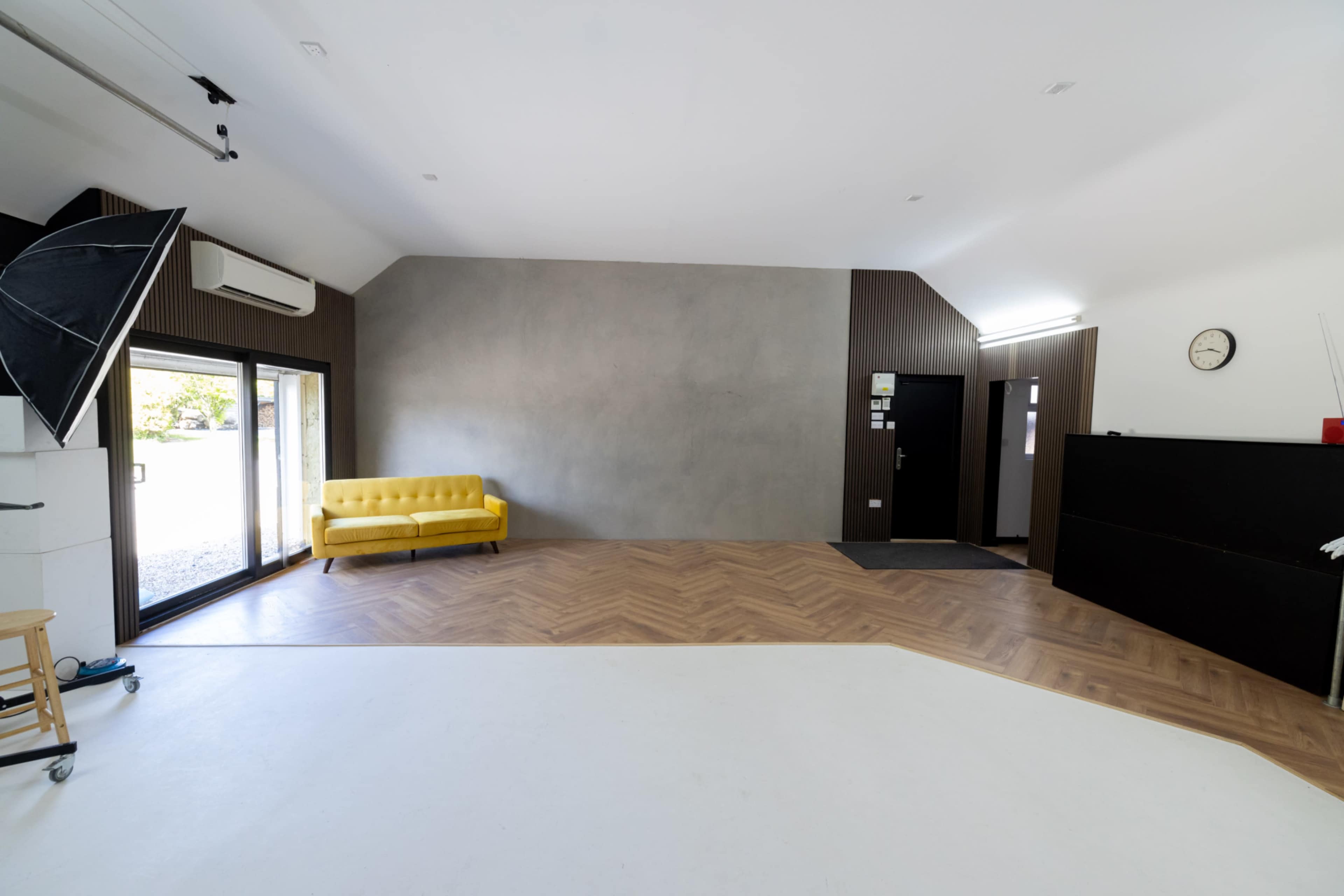 A spacious studio with a yellow sofa, large windows, and a combination of a wood and concrete wall.