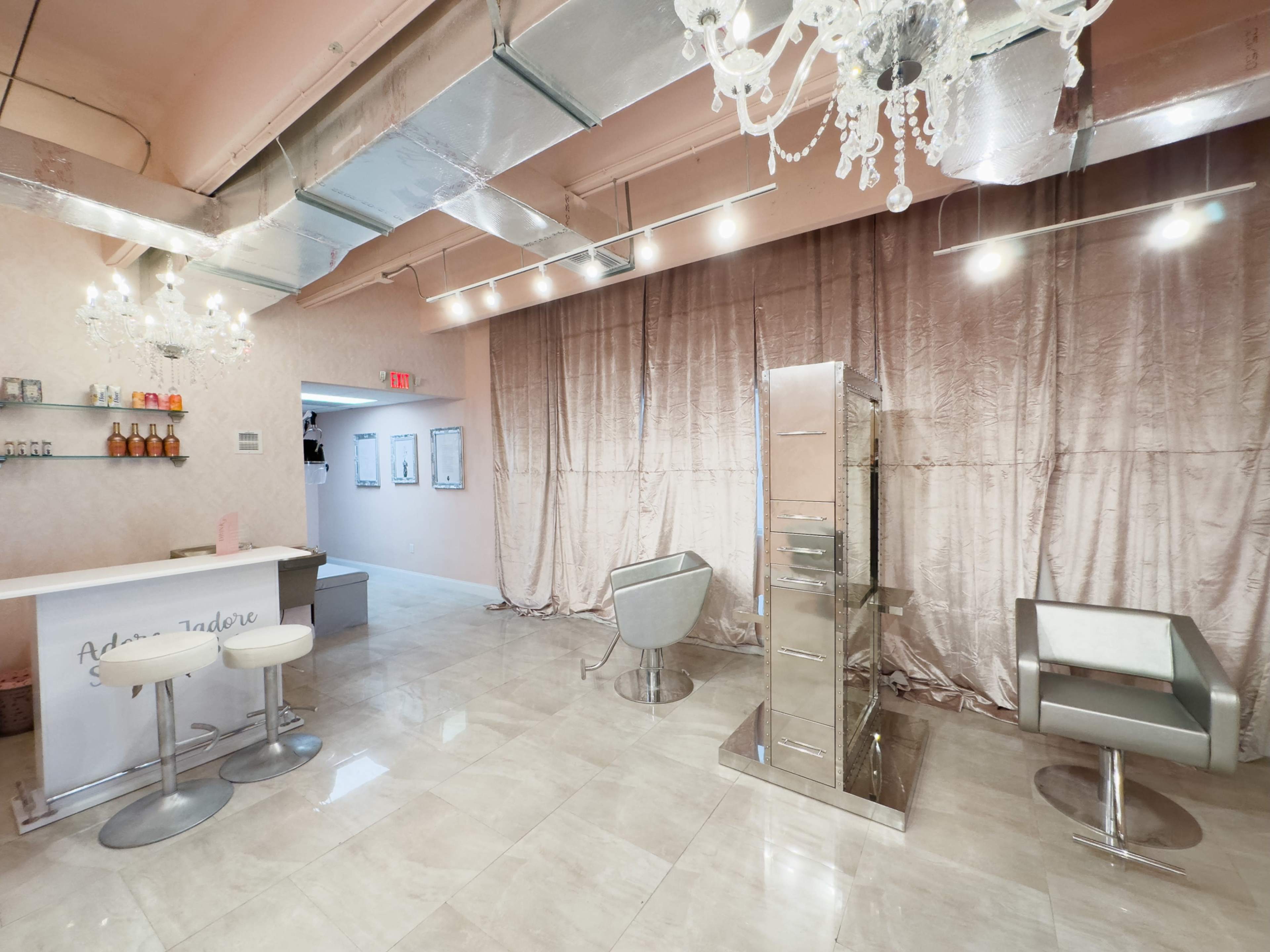 The image shows a modern salon interior with a sleek reception area, stylish chairs, and elegant lighting fixtures.