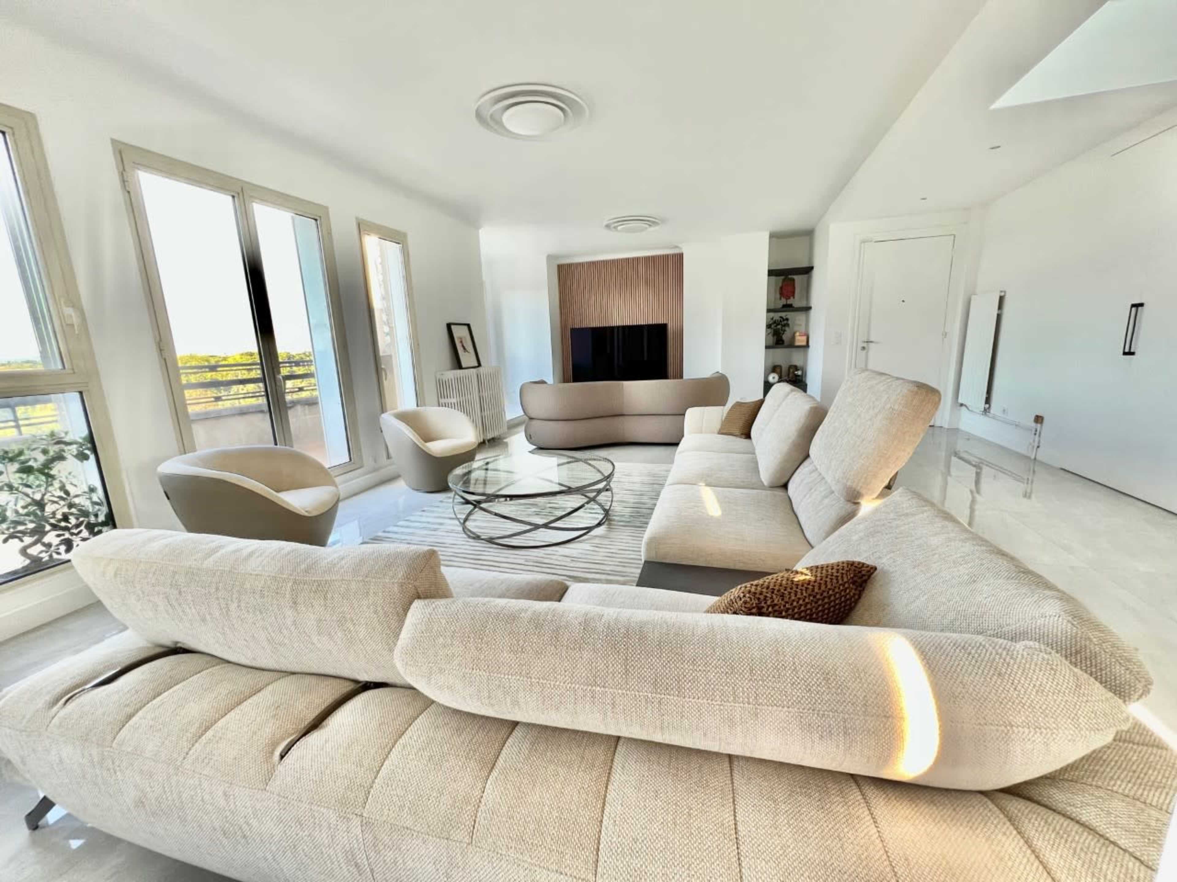 A modern living room with large windows, a circular coffee table, and an L-shaped sofa arrangement.