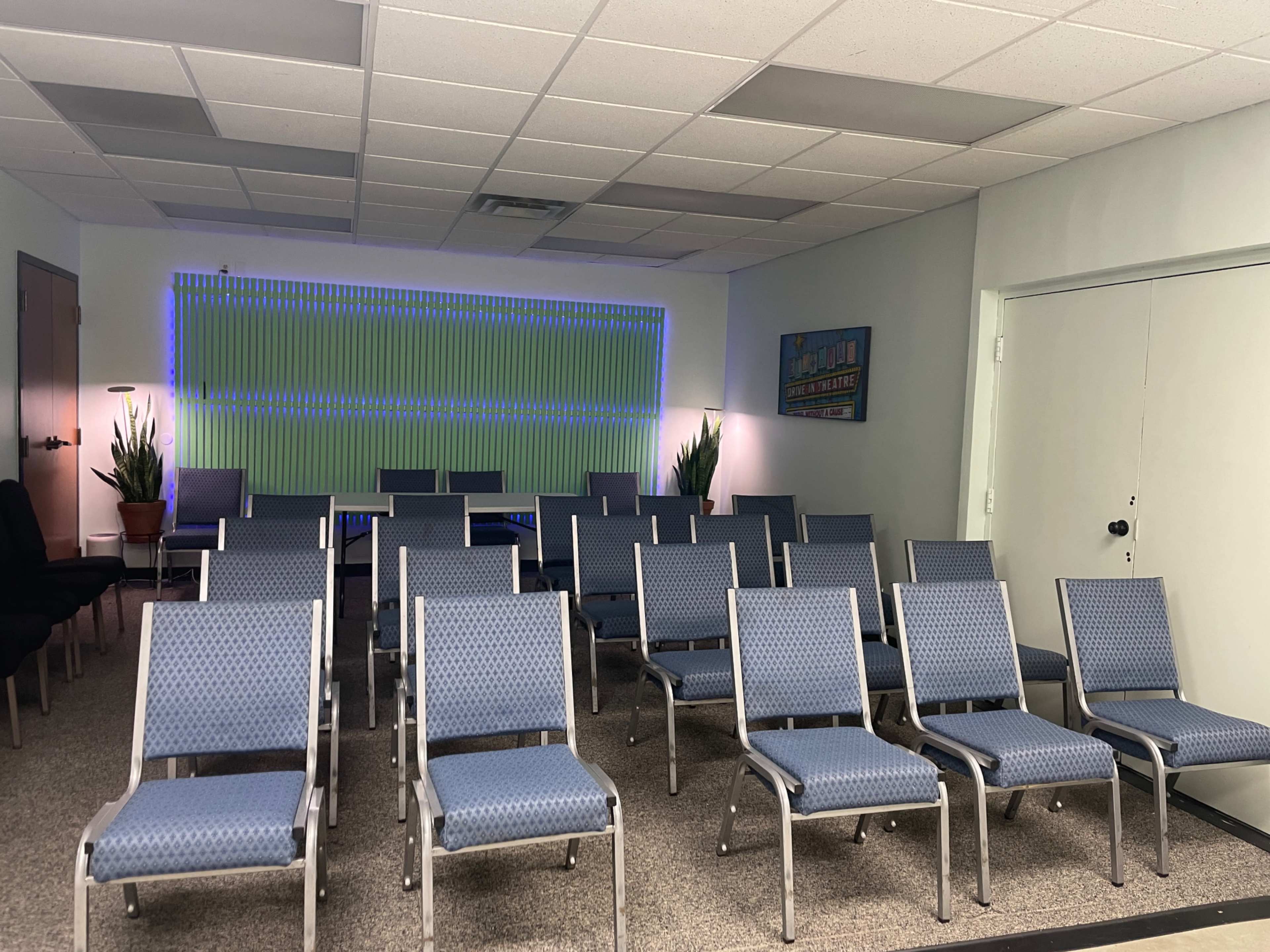 The image shows a meeting room with multiple rows of blue chairs arranged in a grid, complemented by green and blue wall lighting.