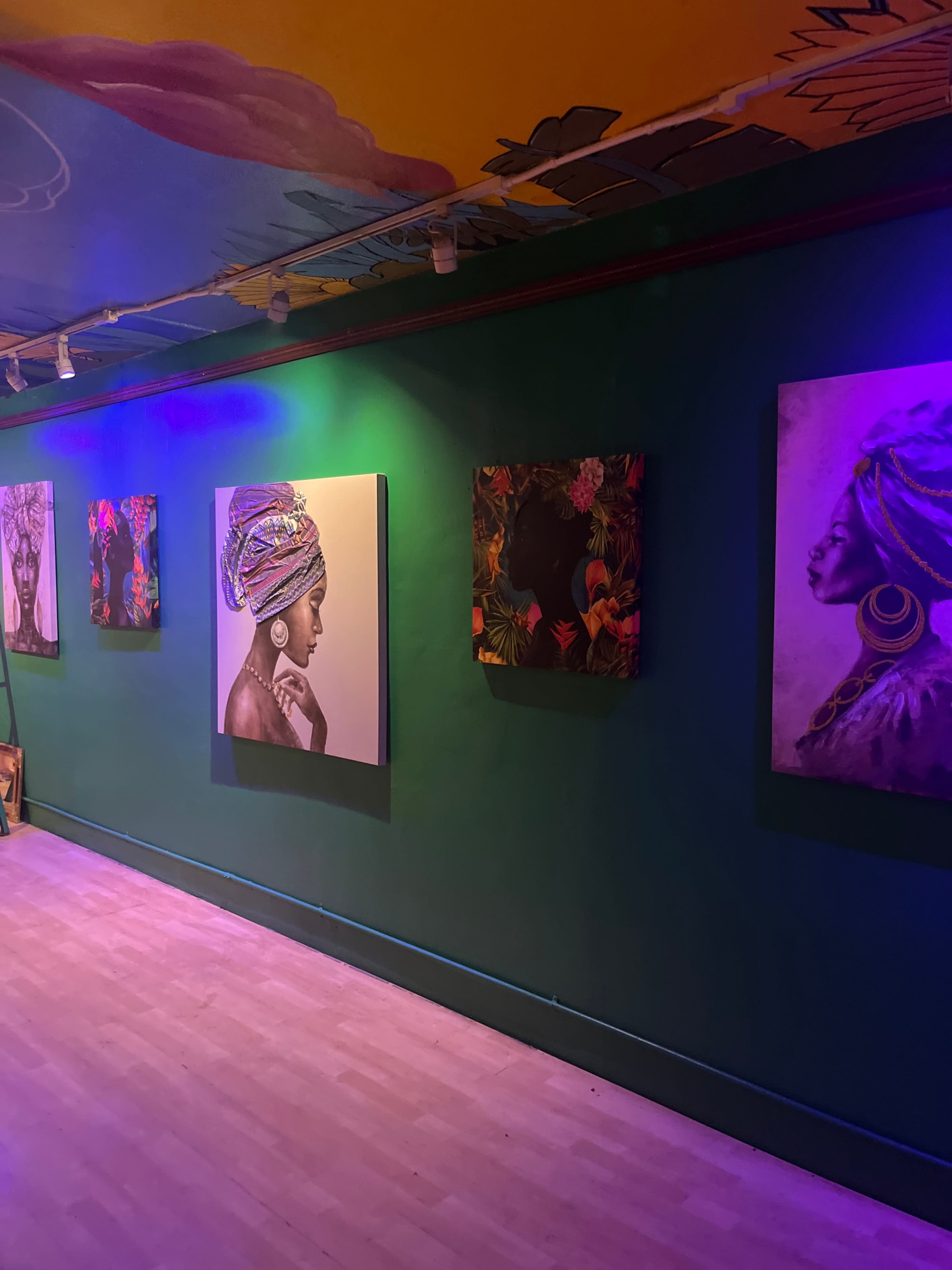 A gallery wall featuring several portraits of women, each depicted in different artistic styles, set against a green wall illuminated with purple lighting.