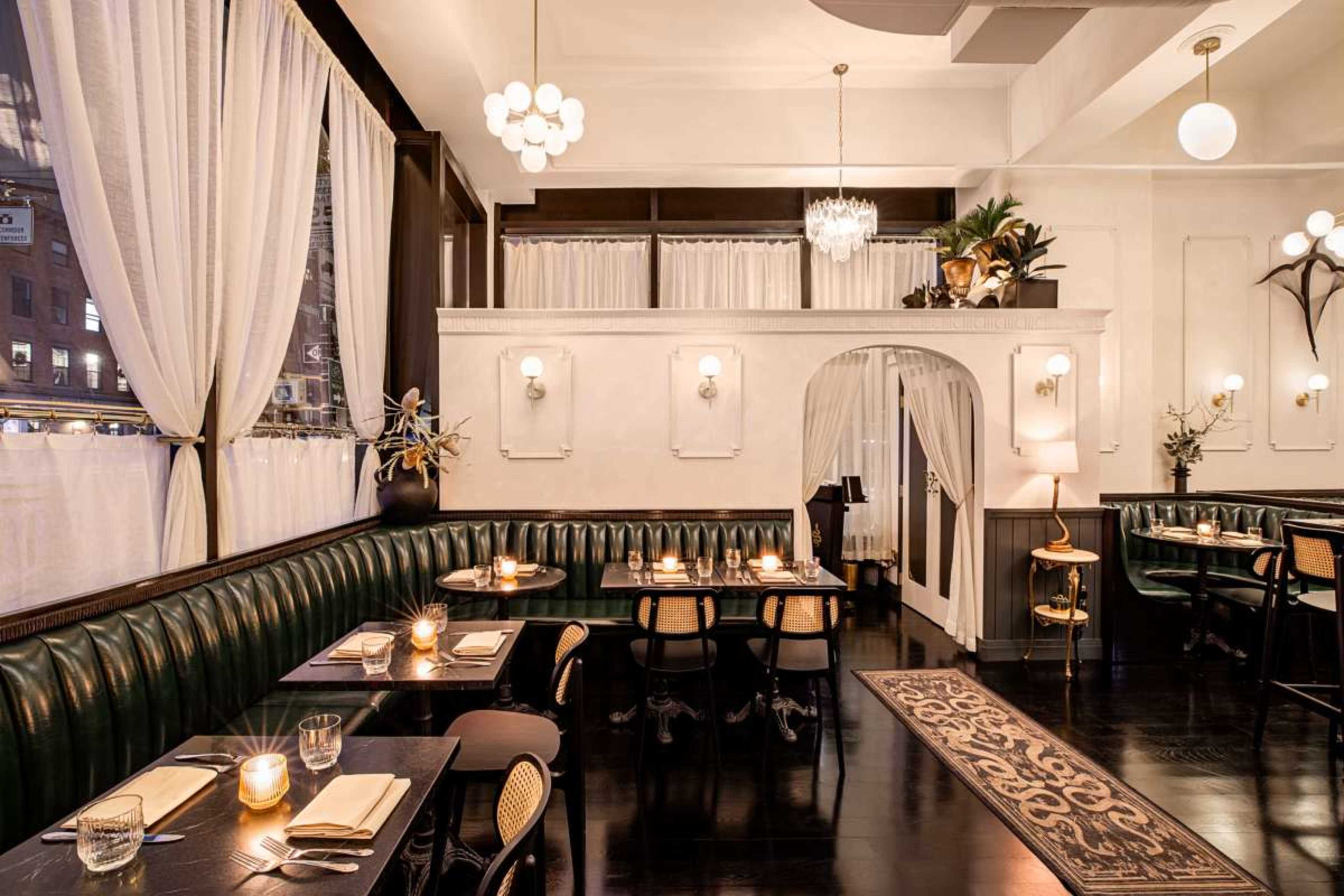The image shows a restaurant interior featuring dark wooden floors, green leather seating, and elegantly set tables with warm lighting.