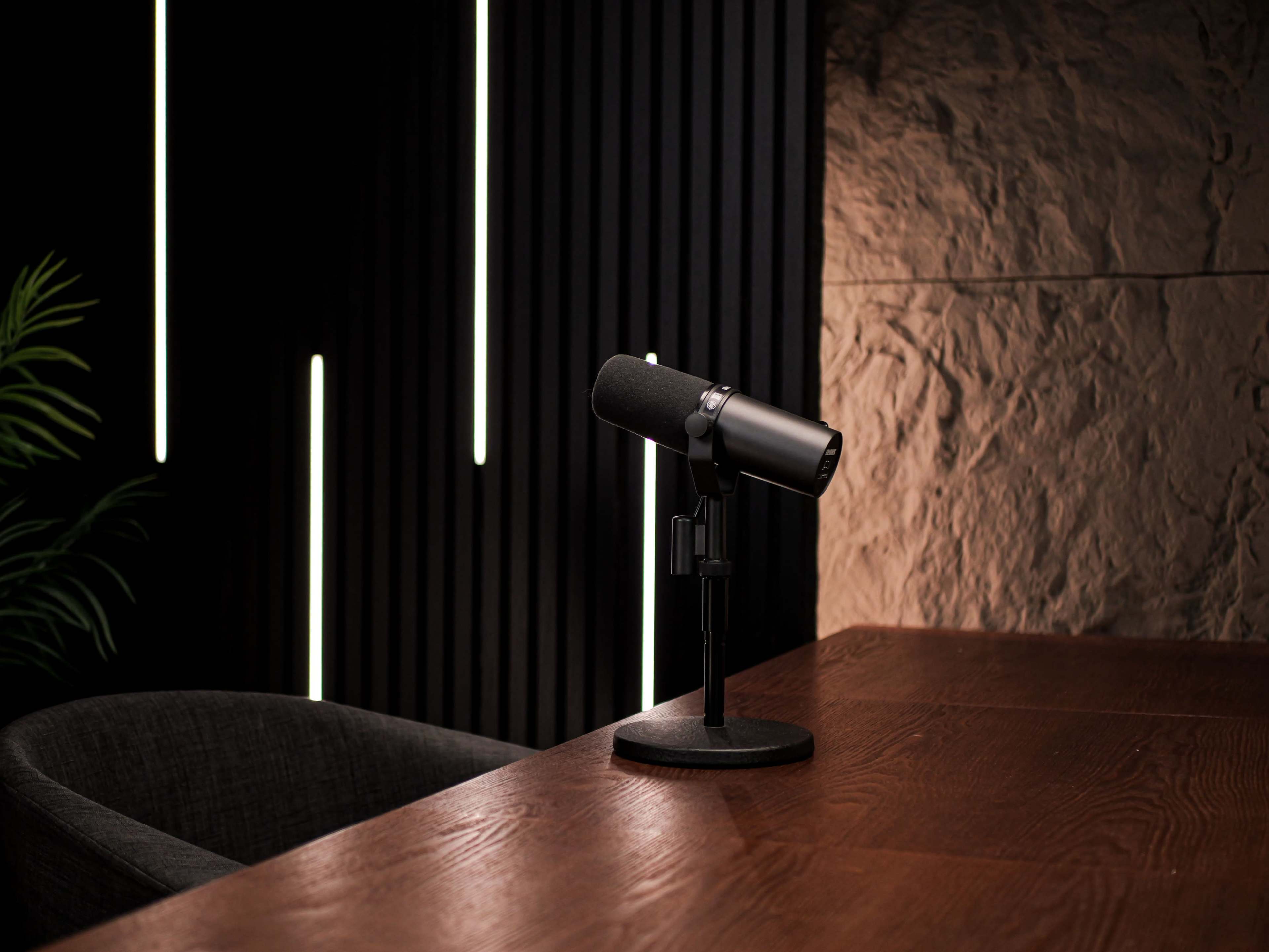 A microphone sits on a wooden table in a dimly lit room with textured walls and vertical light strips.