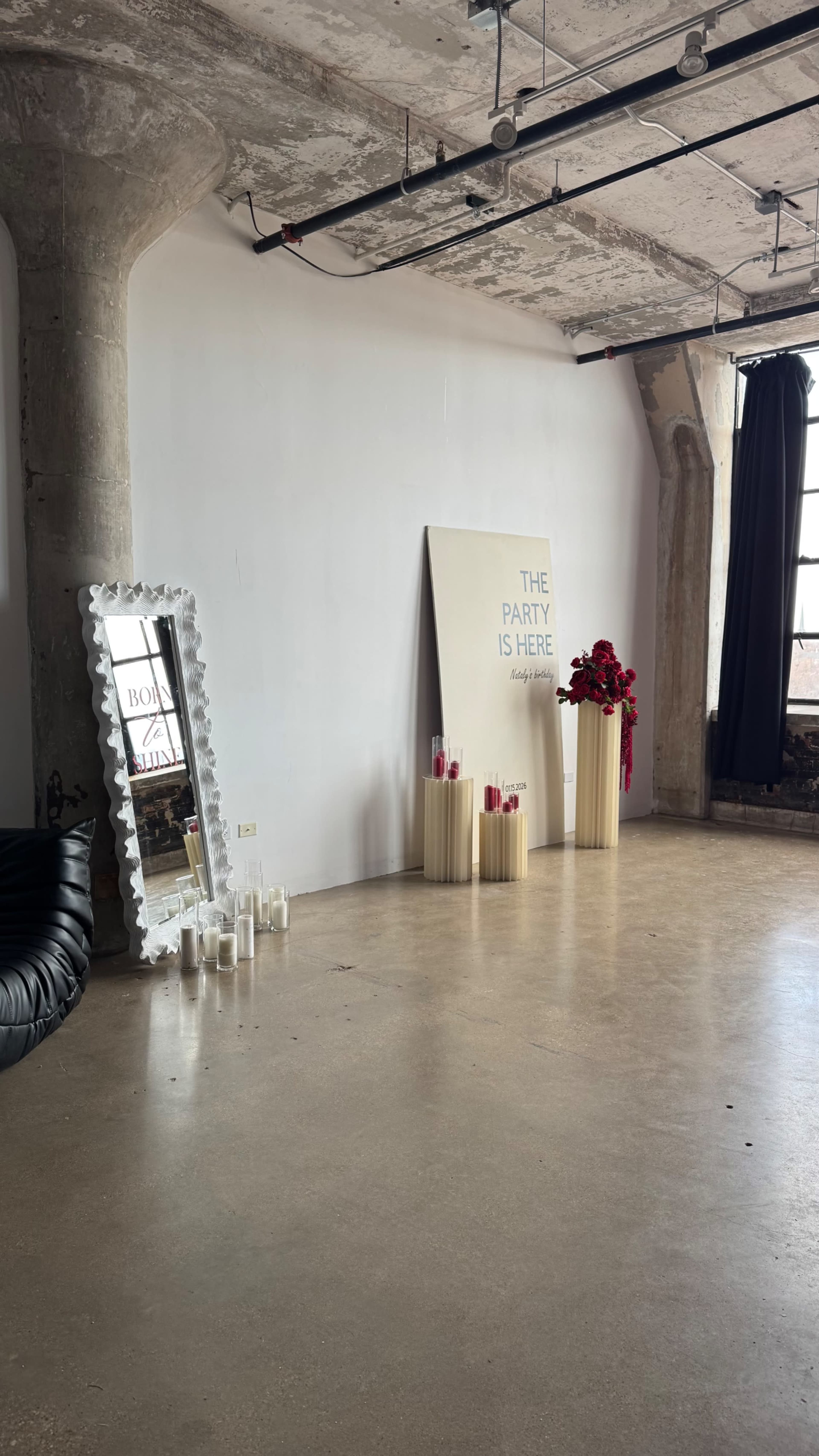 The image shows a spacious, minimalist room with a large mirror, decorative candles, and a wall display that reads "THE PARTY IS HERE."
