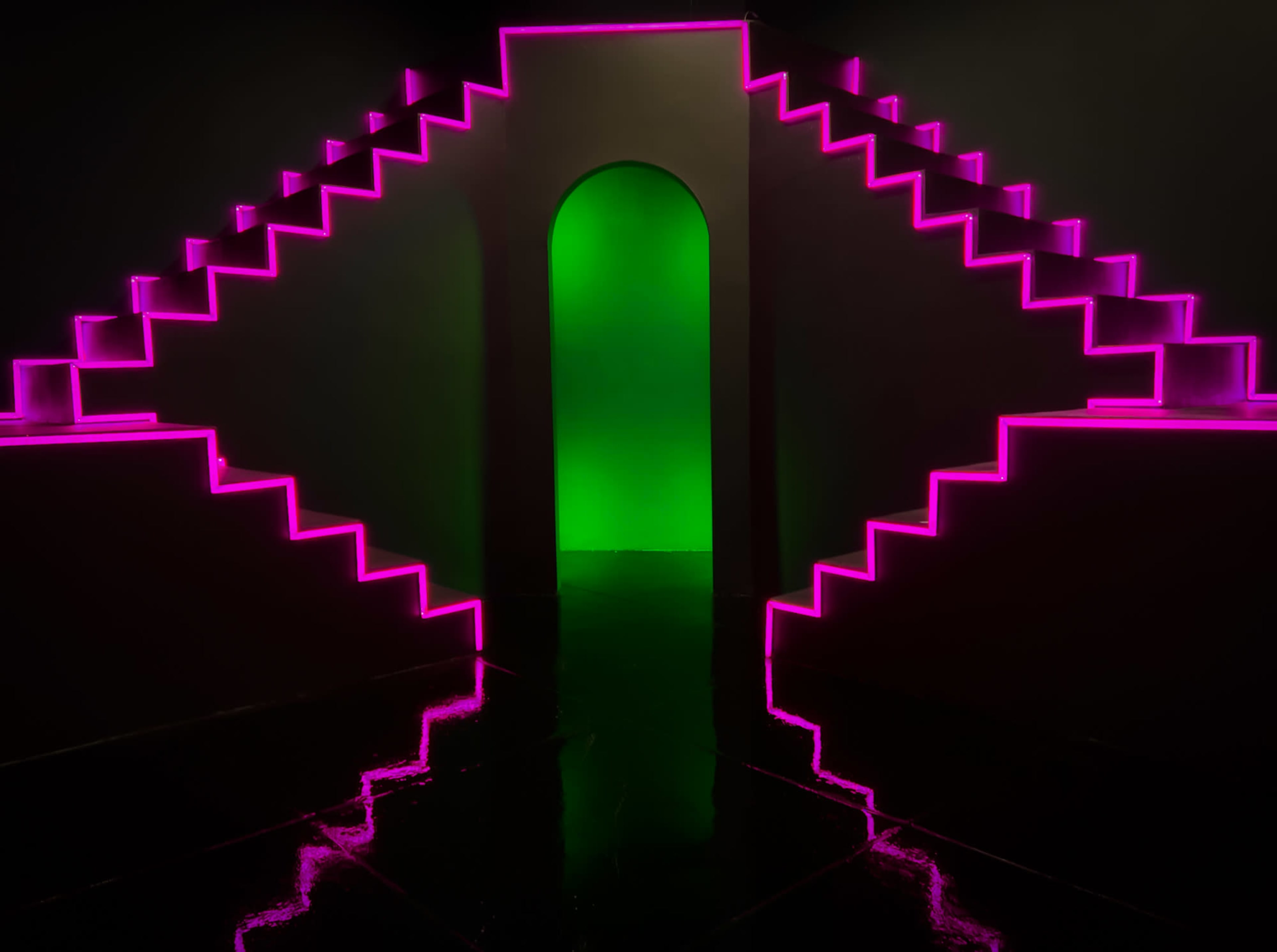 A pair of illuminated pink staircases leads to a green-lit archway against a dark background.