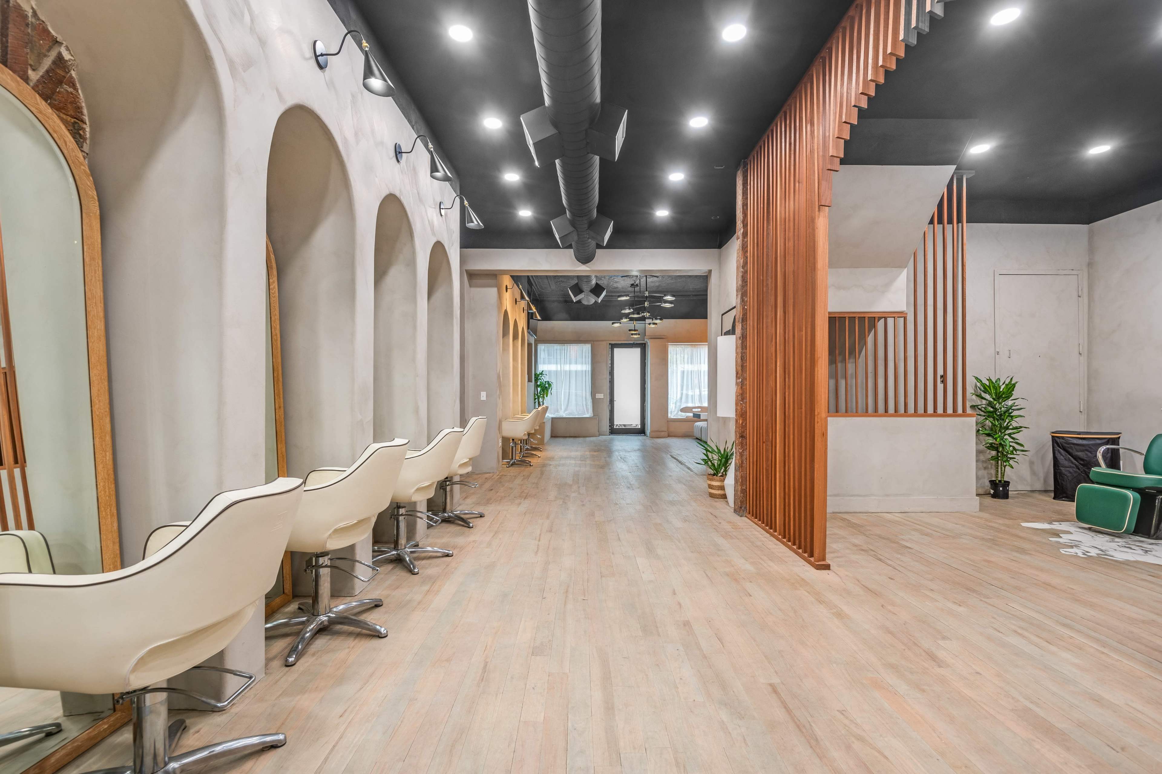 The image shows a modern interior of a salon with curved mirrors, light-colored flooring, and wooden accents.