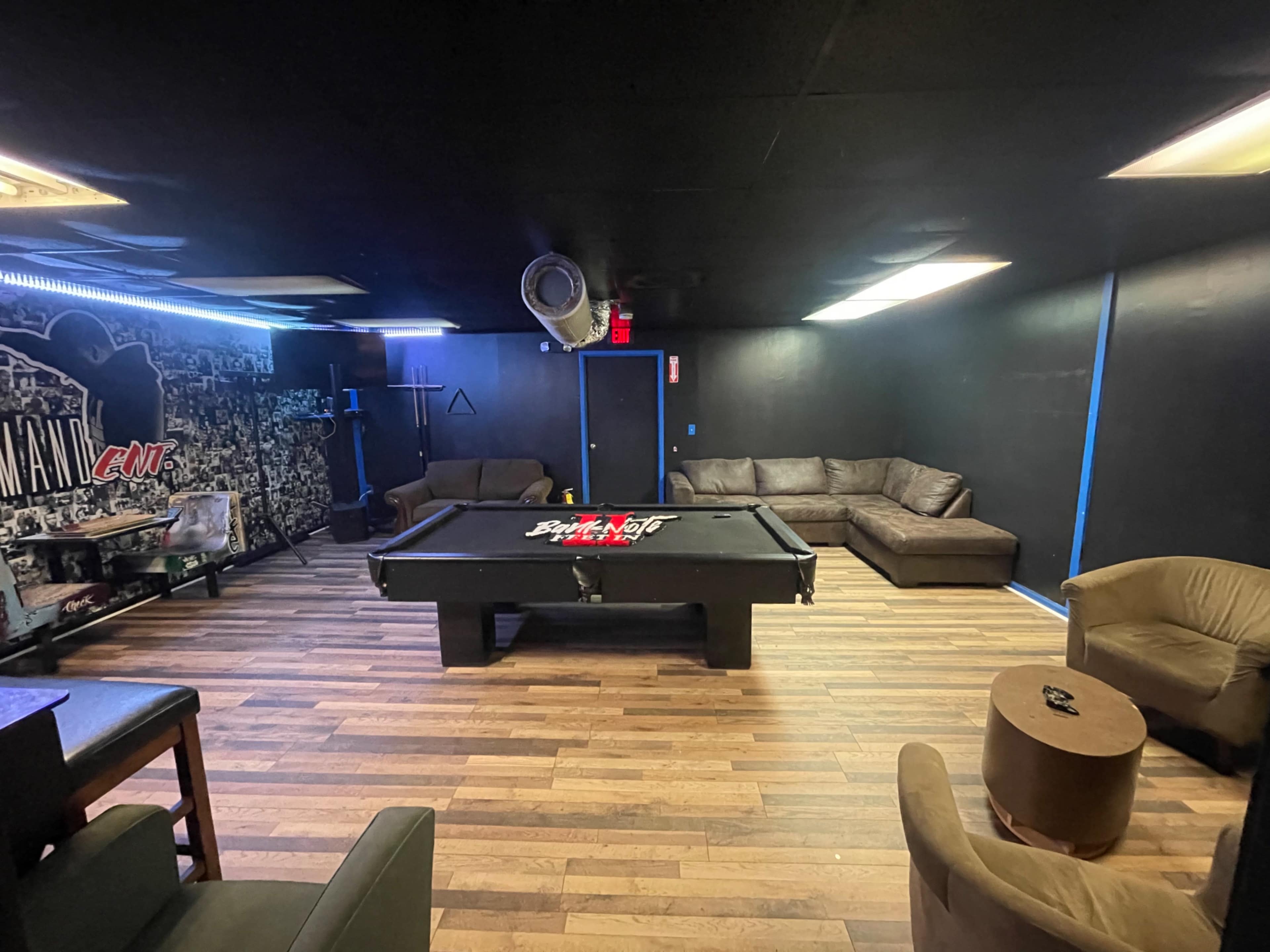 A dark room with a pool table in the center, surrounded by couches and a coffee table.