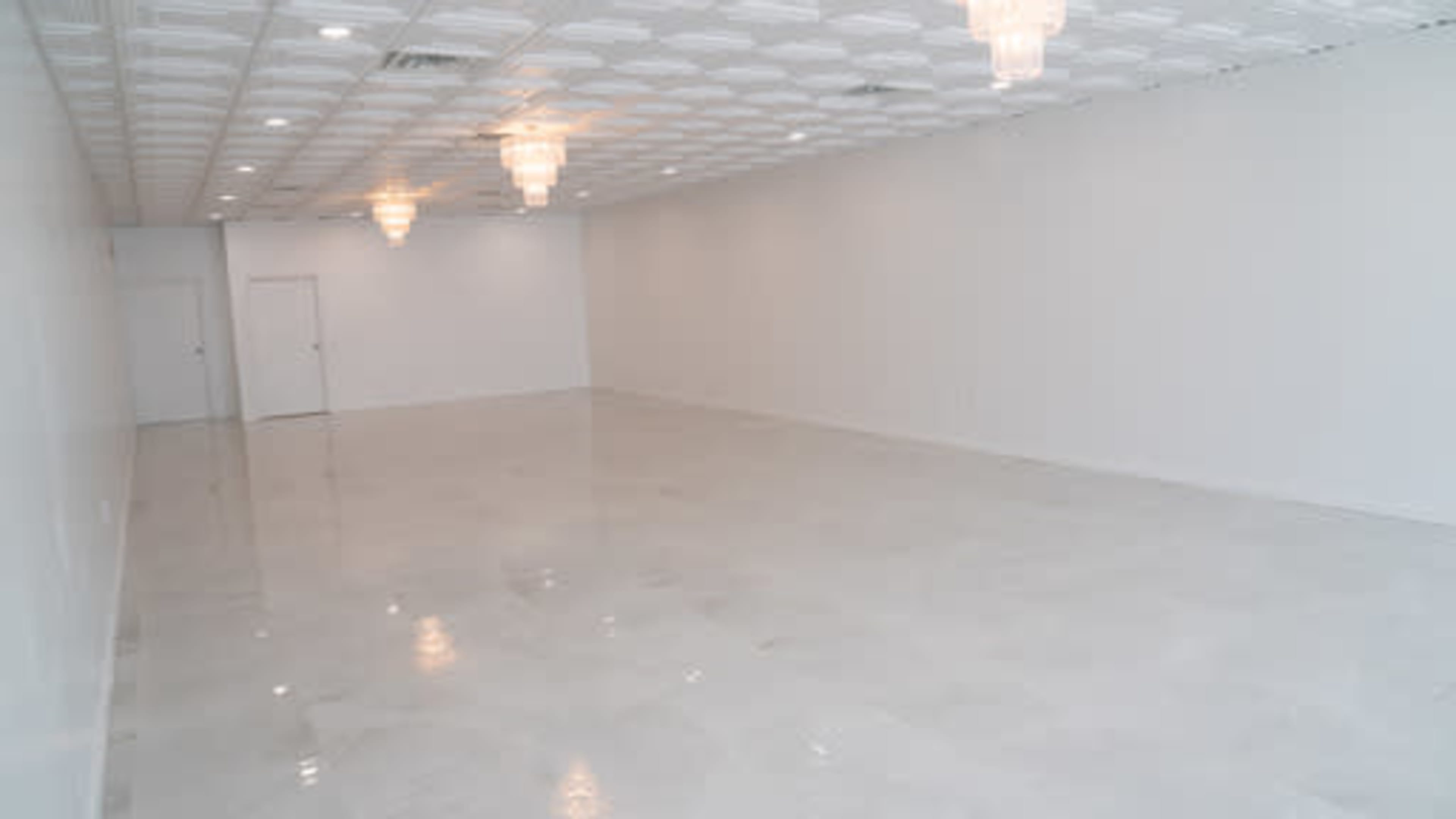The image shows a spacious, empty room with white walls and a glossy floor, featuring two hanging light fixtures.