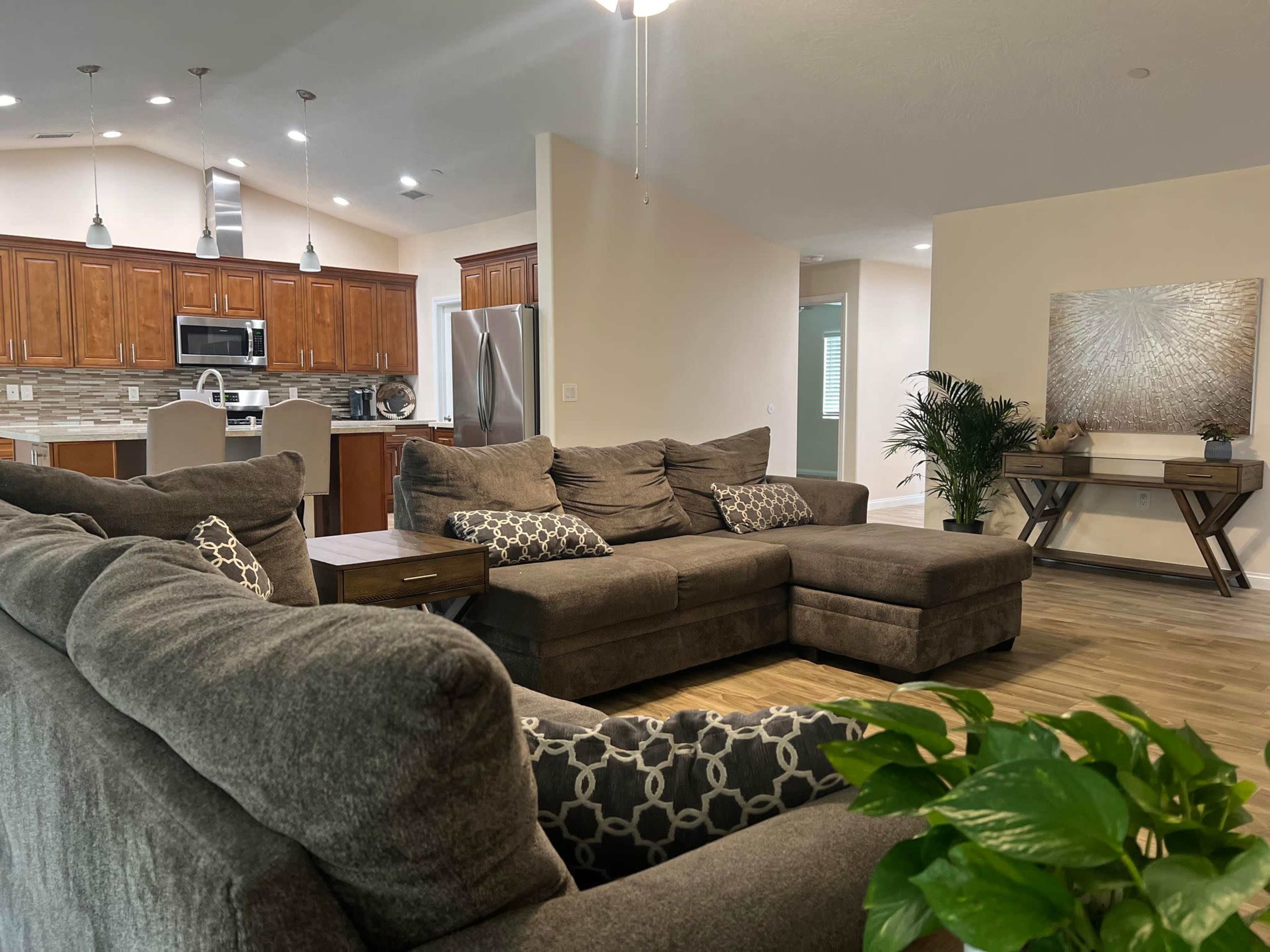 A spacious living room with two gray sofas facing each other, a wooden coffee table in the center, and a kitchen visible in the background.