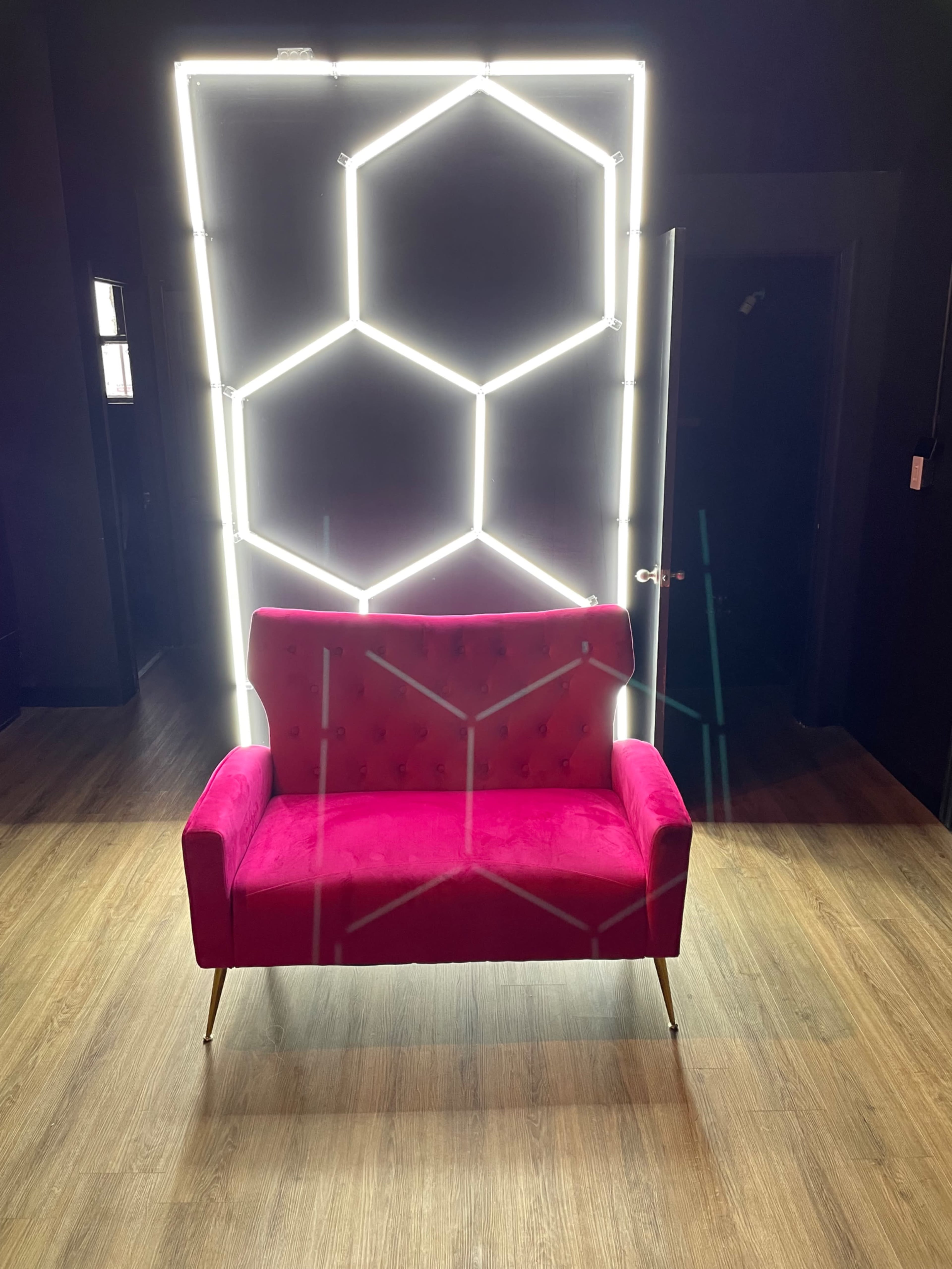 A pink tufted sofa is positioned in front of a lit neon geometric panel against a dark background.