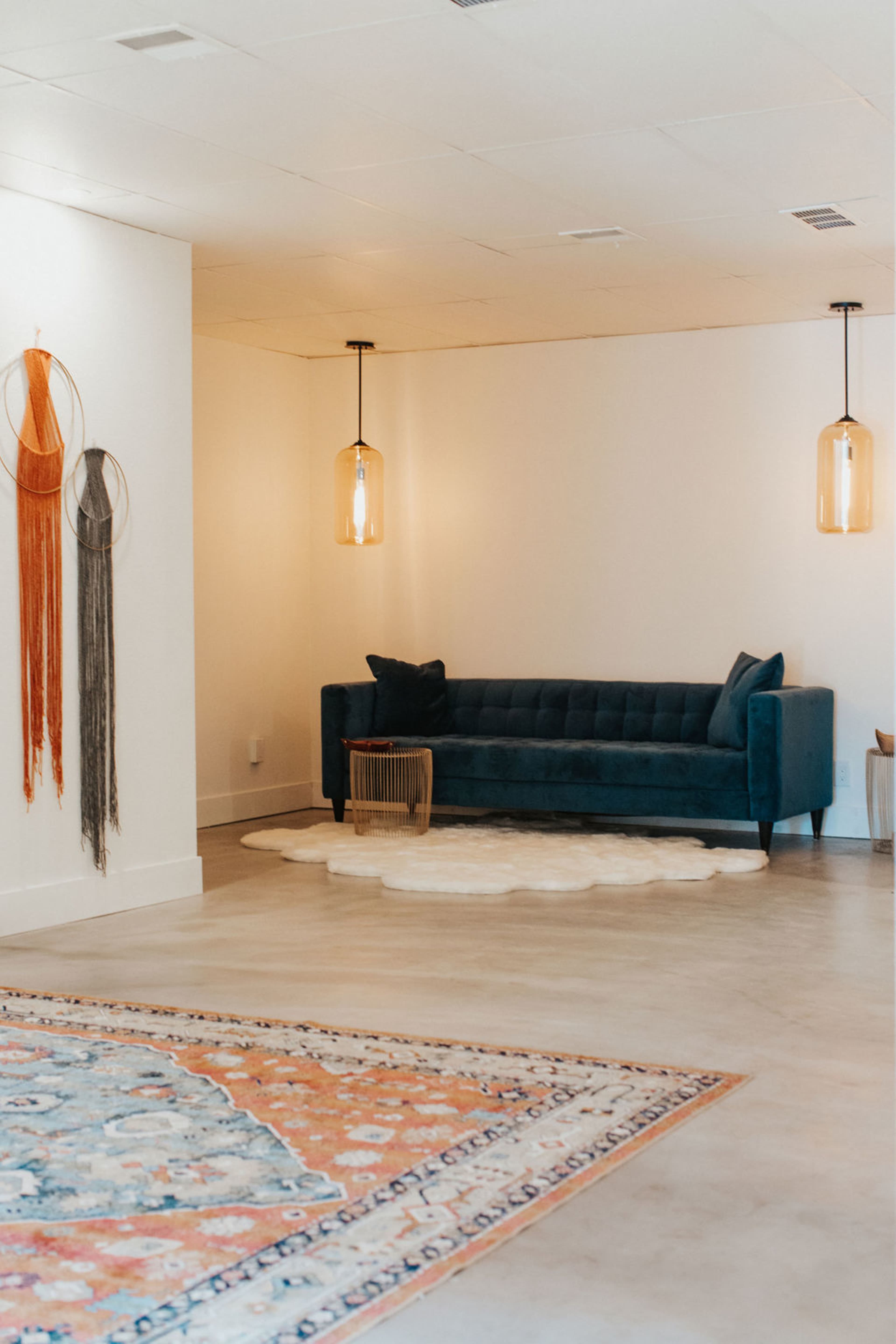 A modern interior space featuring a blue velvet sofa, a decorative rug, and hanging pendant lights.
