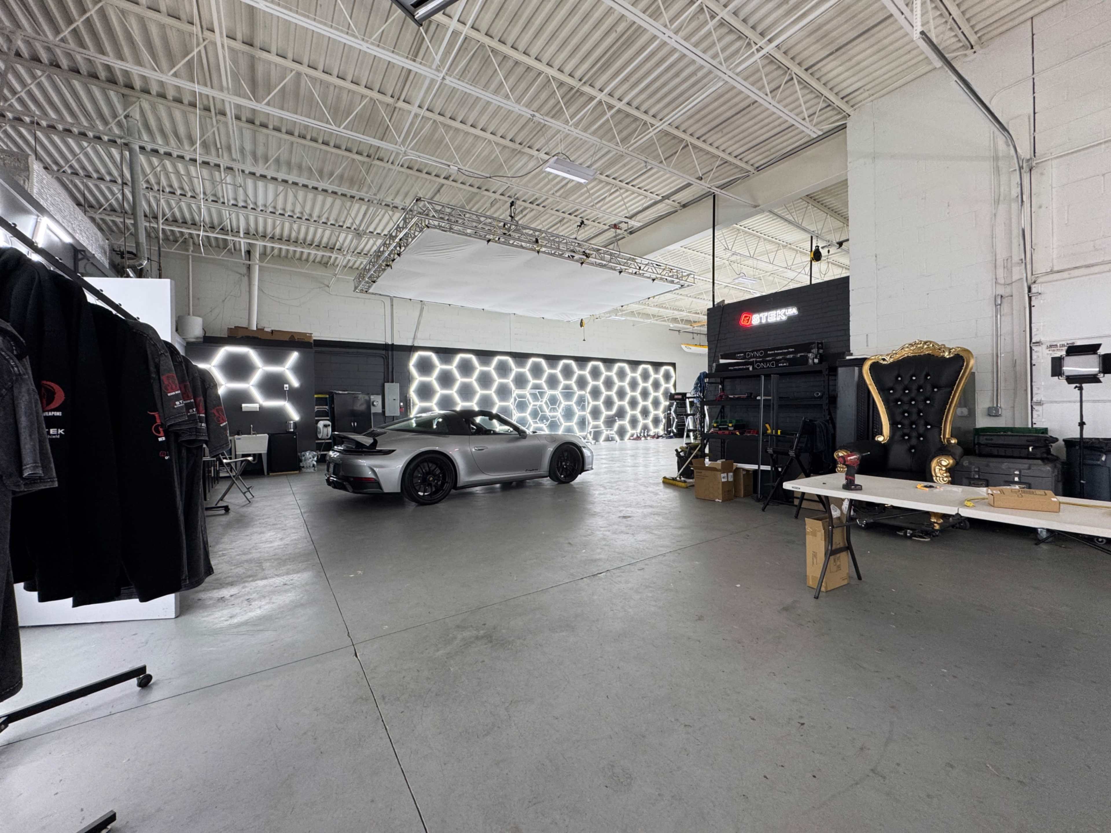 A sleek gray sports car is positioned in a modern studio space adorned with hexagonal lighting and various equipment.