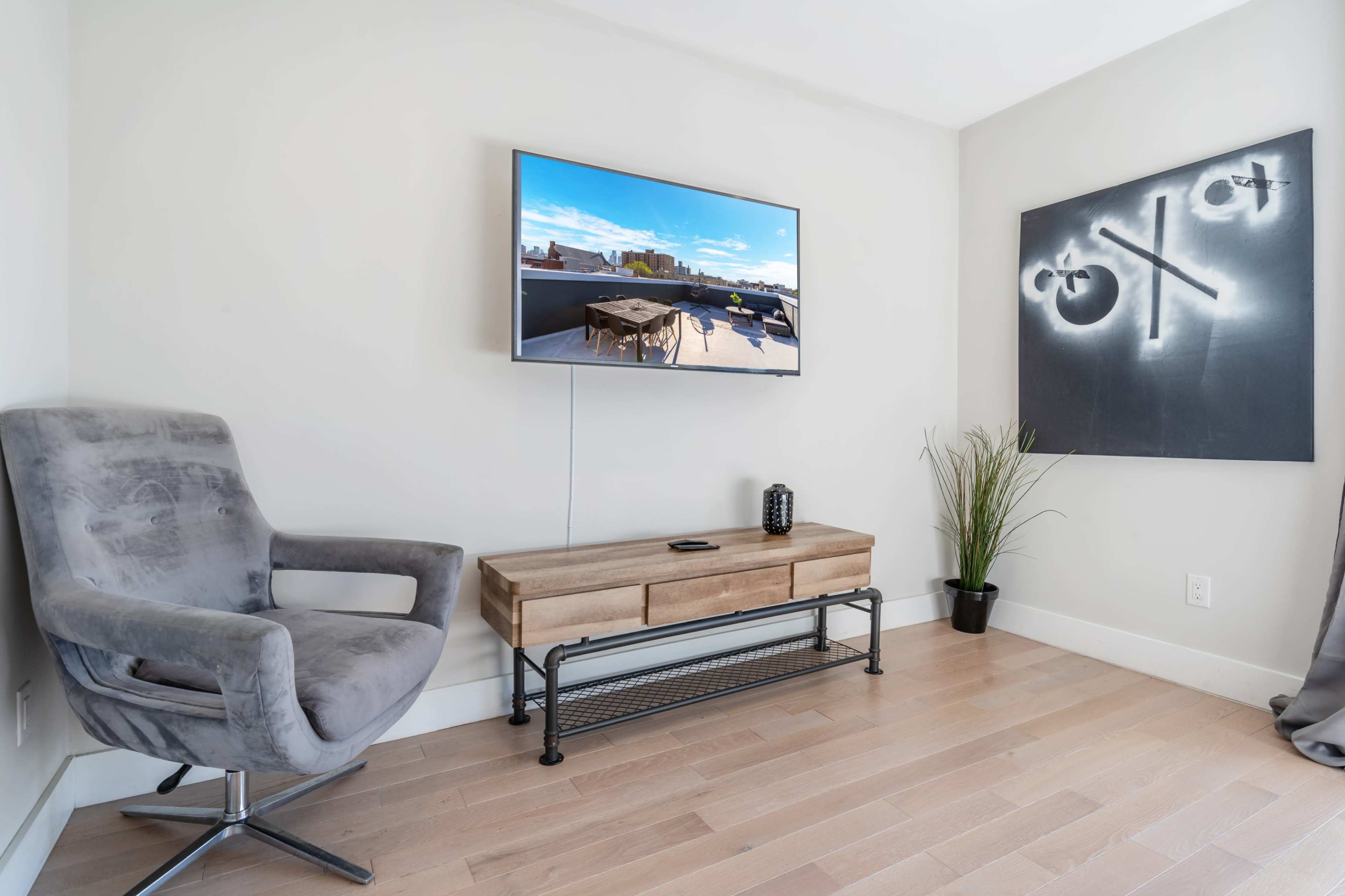 A gray armchair and wooden TV stand are positioned in a minimalist living space featuring a mounted television and a decorative plant.