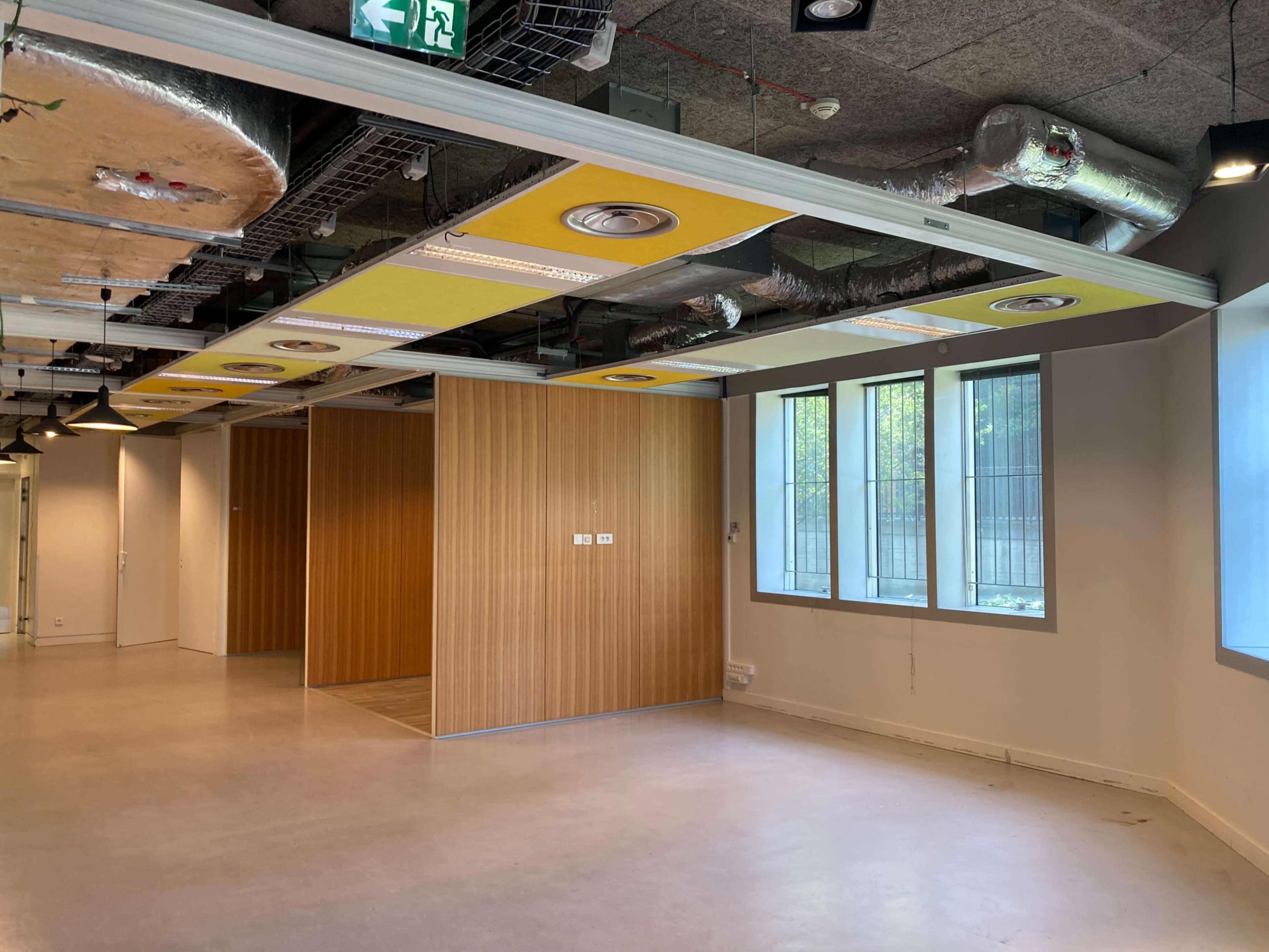 The image shows an empty office space with wooden paneling and large windows, featuring exposed ceilings and ductwork.