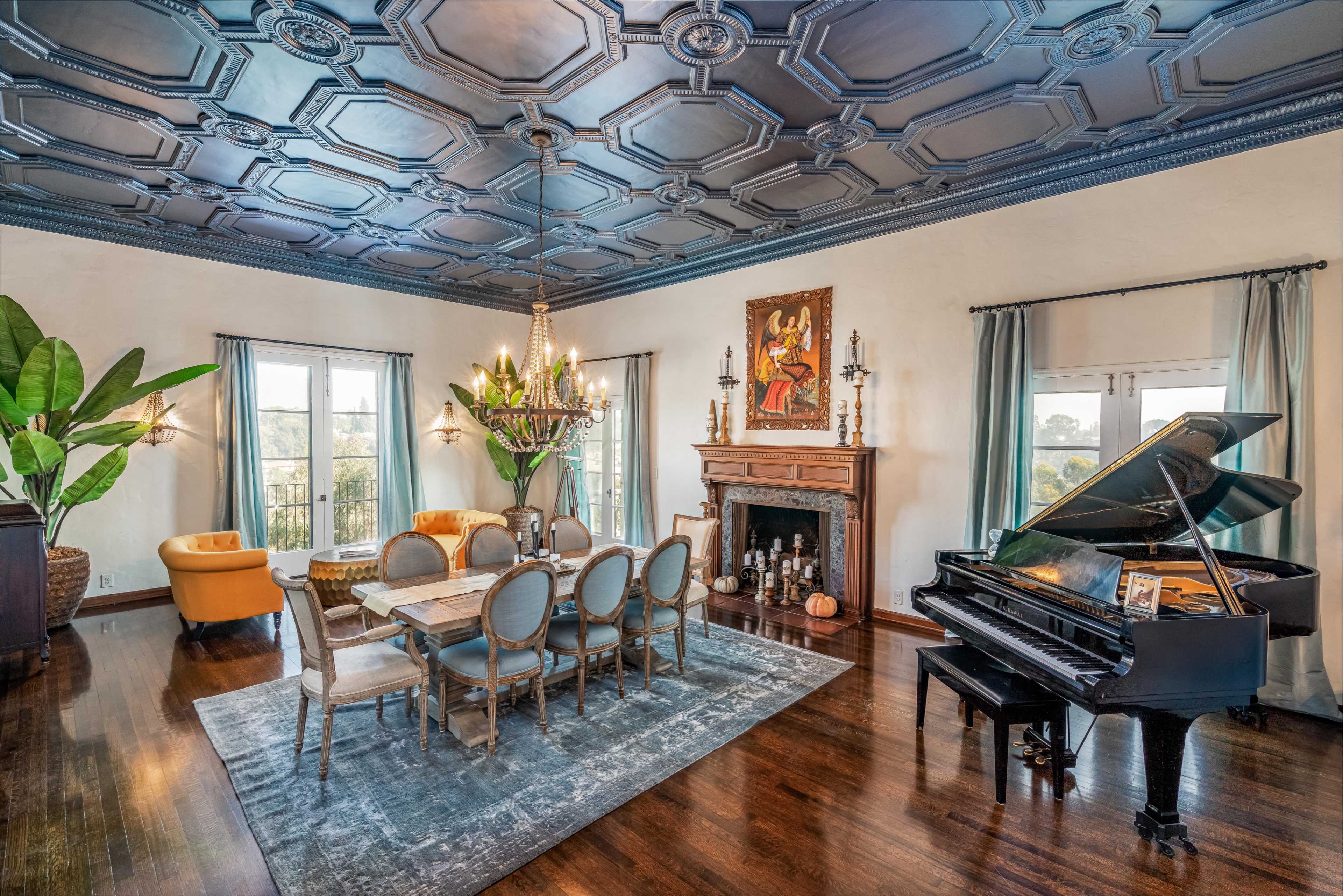 An elegantly furnished dining room with a grand piano, a large chandelier, and a ceiling featuring intricate blue designs.