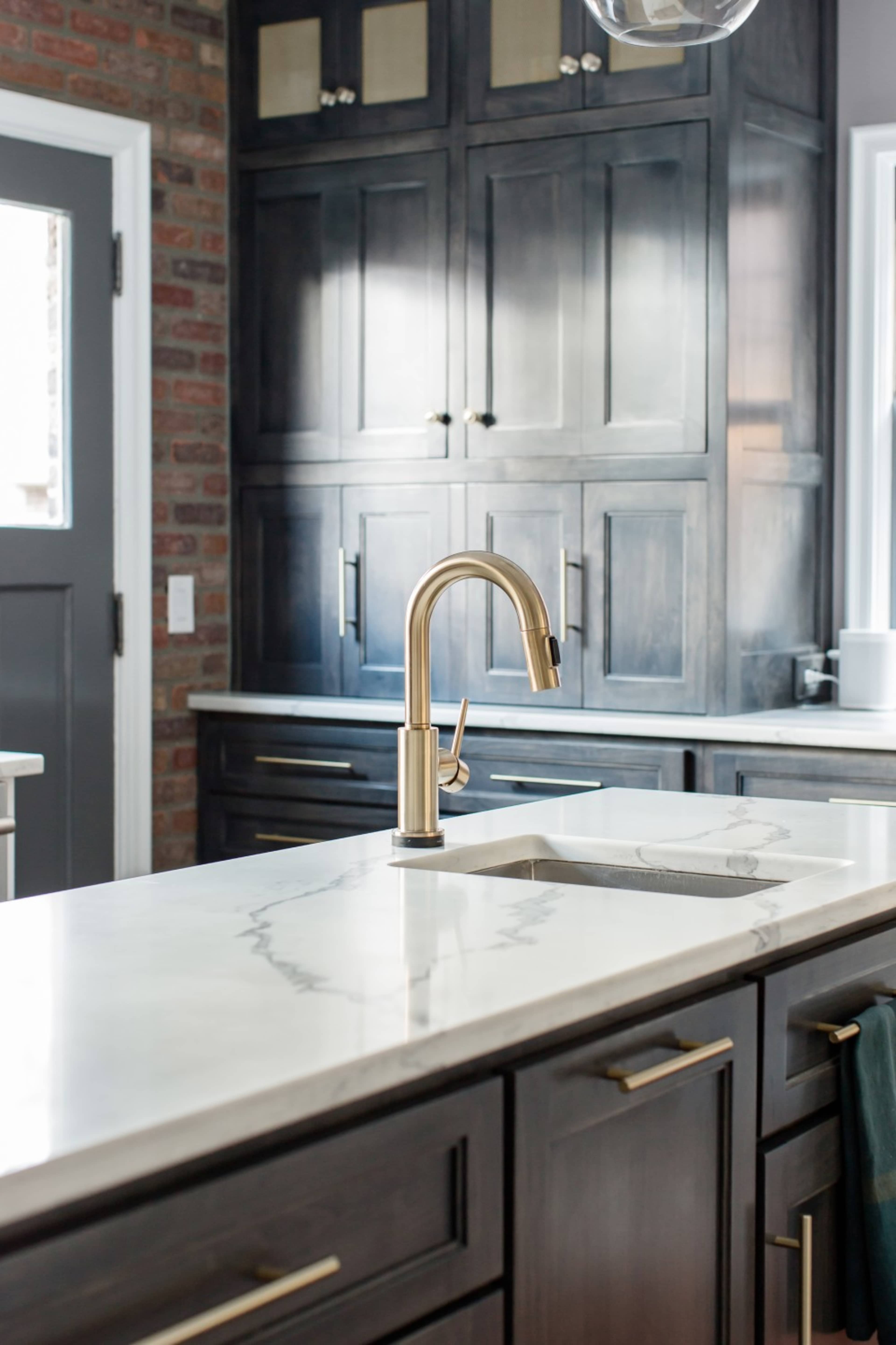 A modern kitchen features dark cabinets, a marble countertop, and a brass faucet.