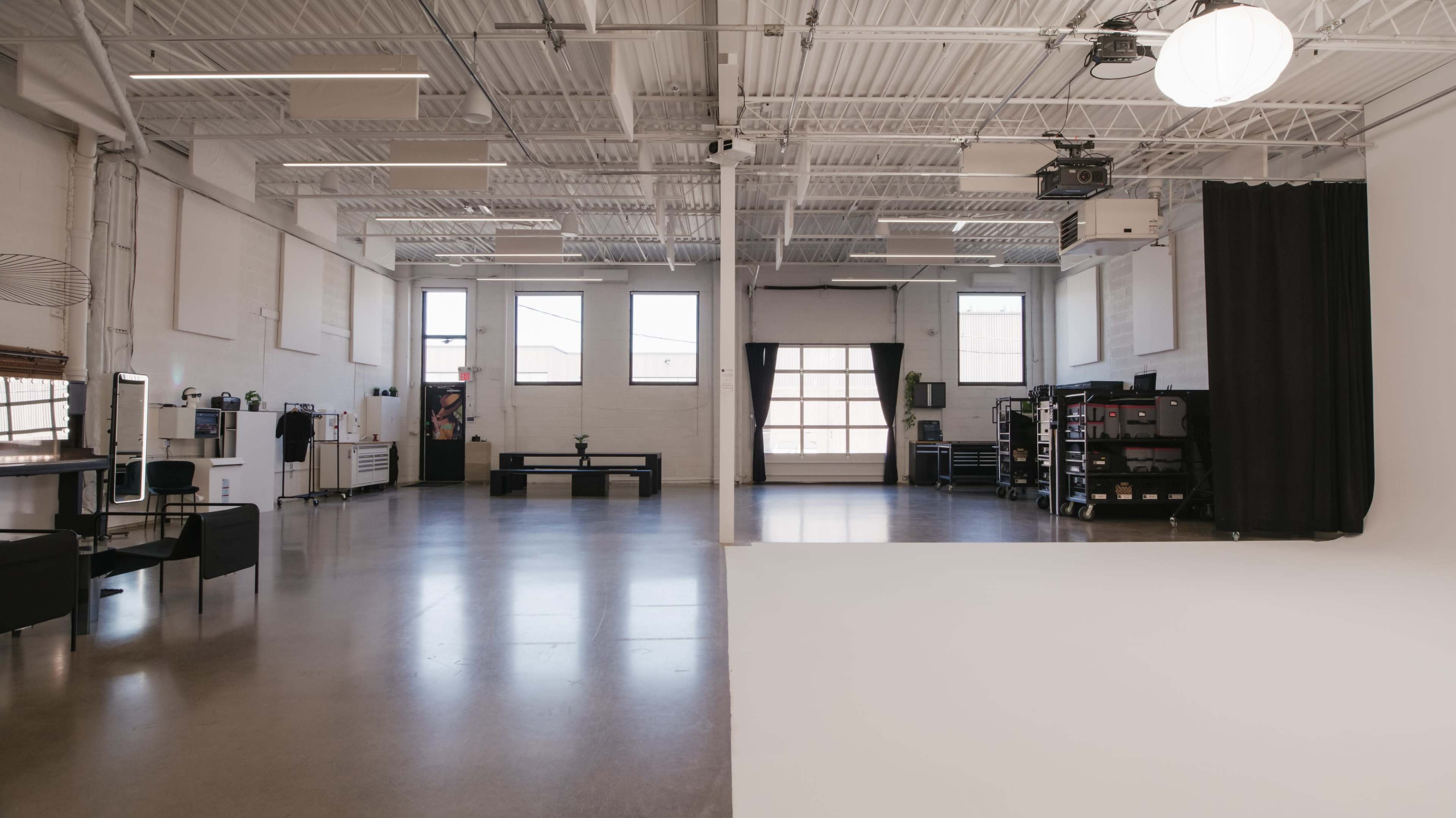 The image depicts a spacious interior studio with polished concrete flooring, large windows, and various equipment along the walls.
