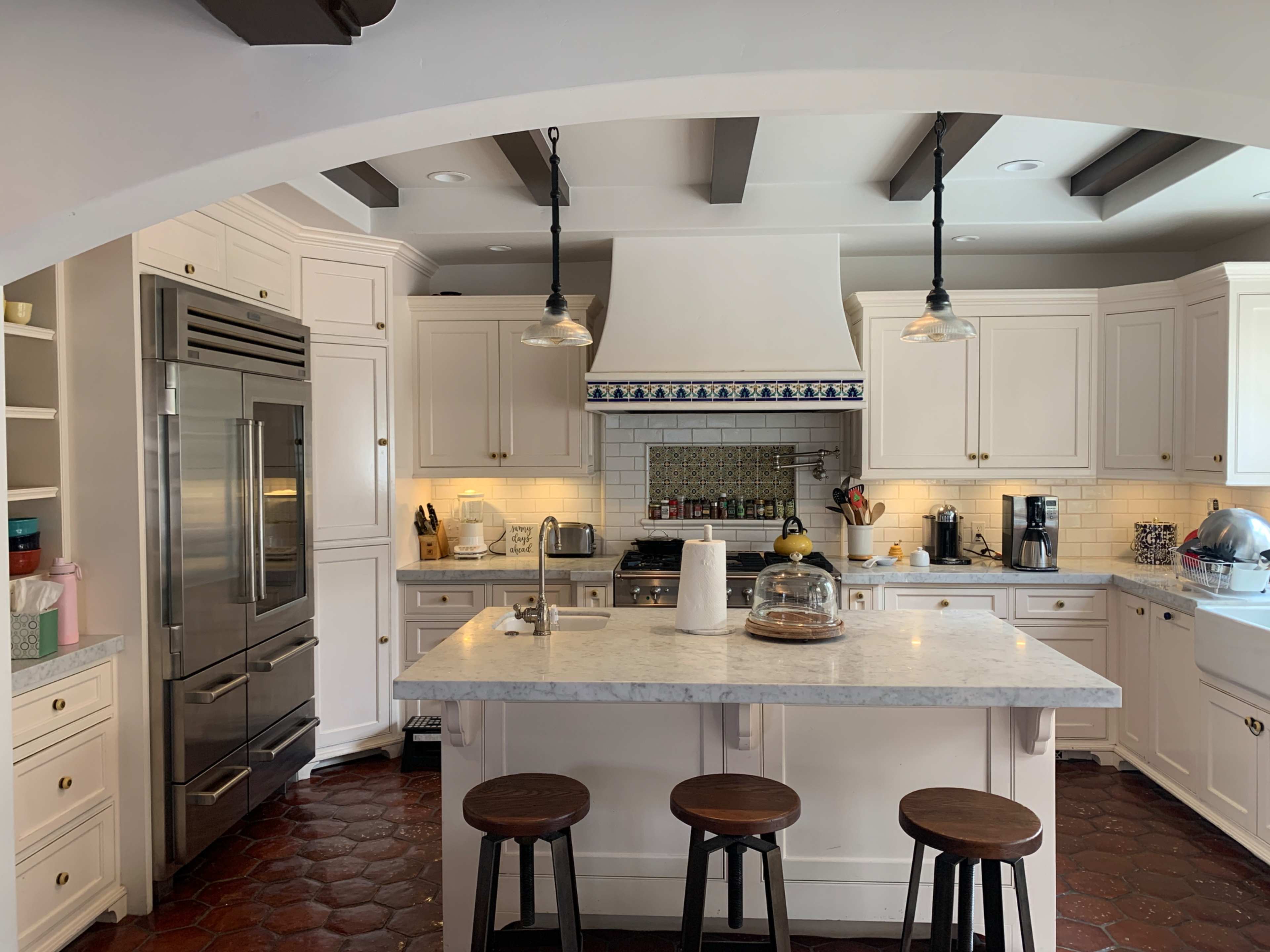 A spacious kitchen featuring white cabinets, a large marble island, and a tile backsplash with an archway leading into the room.