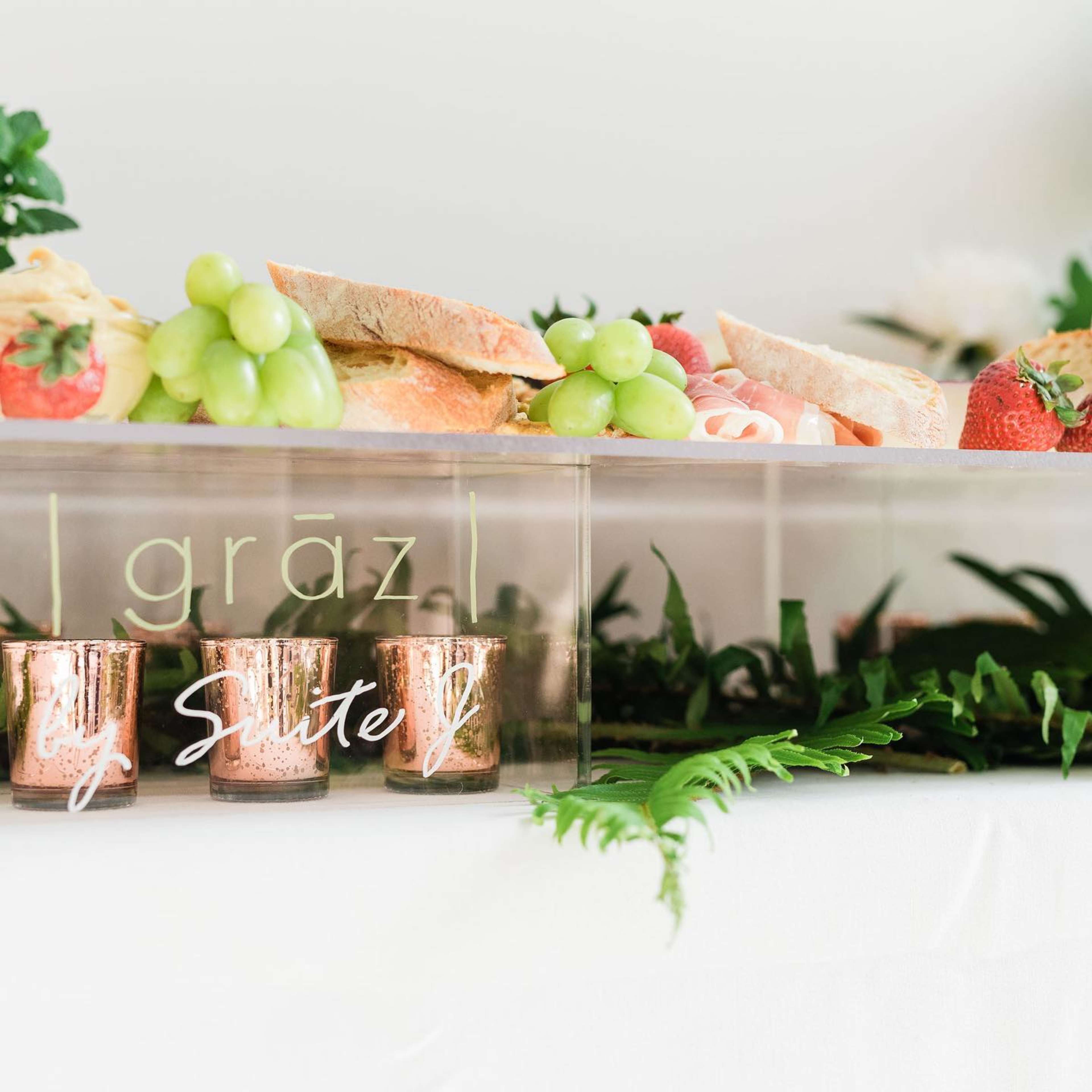 A clear serving display features an assortment of bread, grapes, strawberries, and decorative candles.