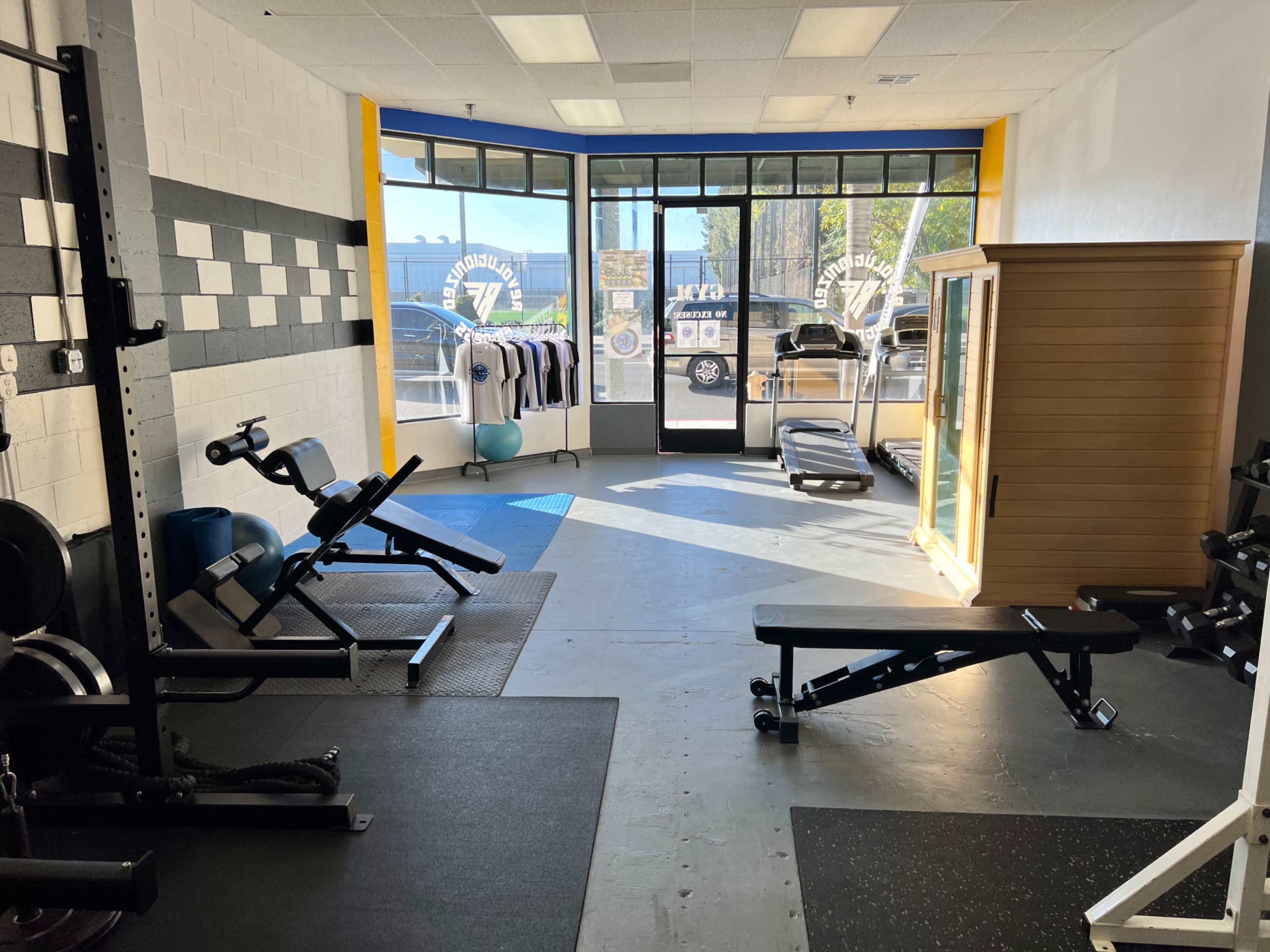 A fitness studio with various gym equipment, including weights and benches, and large windows letting in natural light.