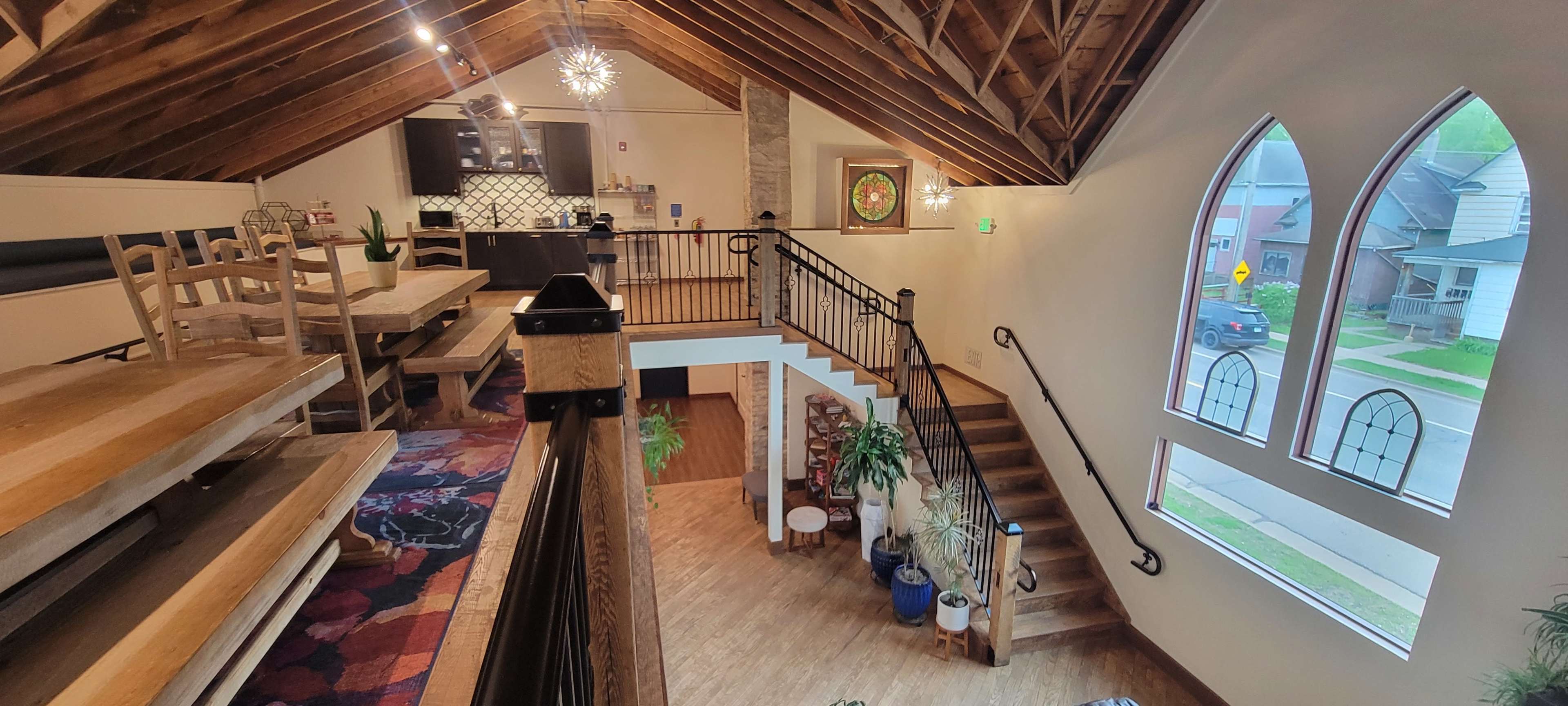 The image shows an interior space with a lofted area featuring wooden beams, a staircase leading to the lower level, and a kitchen area visible in the background.