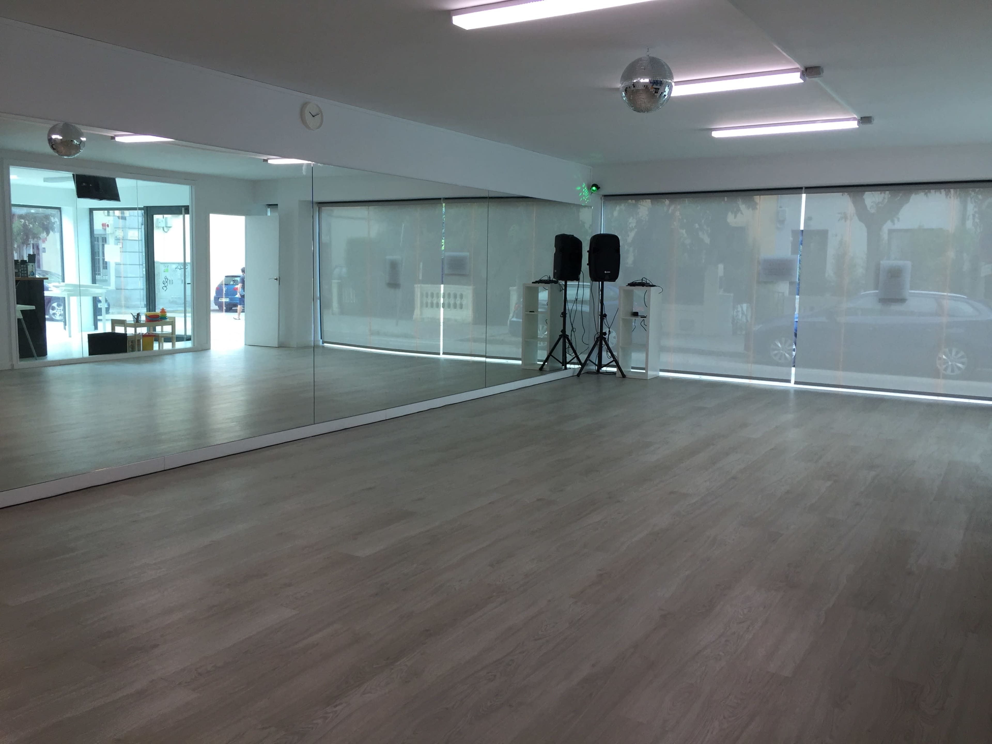 A spacious dance studio with large mirrors on one wall, wooden flooring, and speakers positioned on a stand.