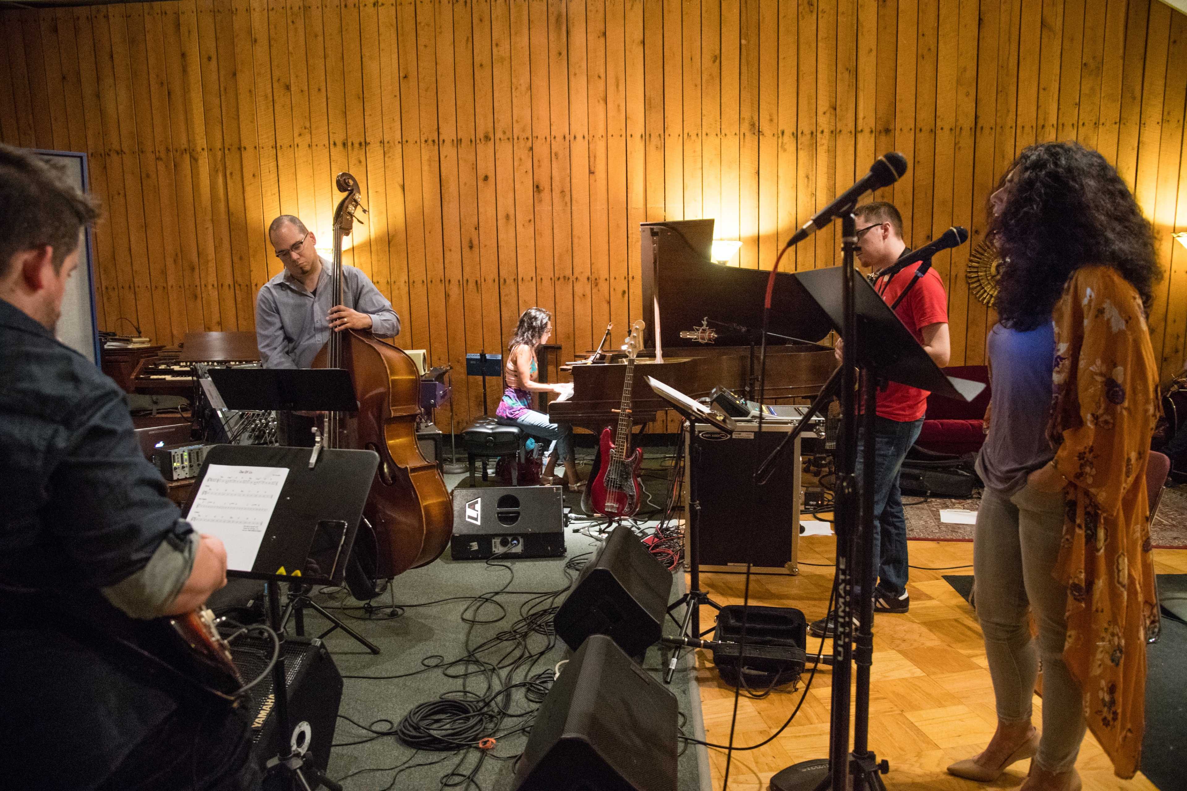 A jazz band performs in a studio setting with a singer, piano player, bassist, and guitarist.