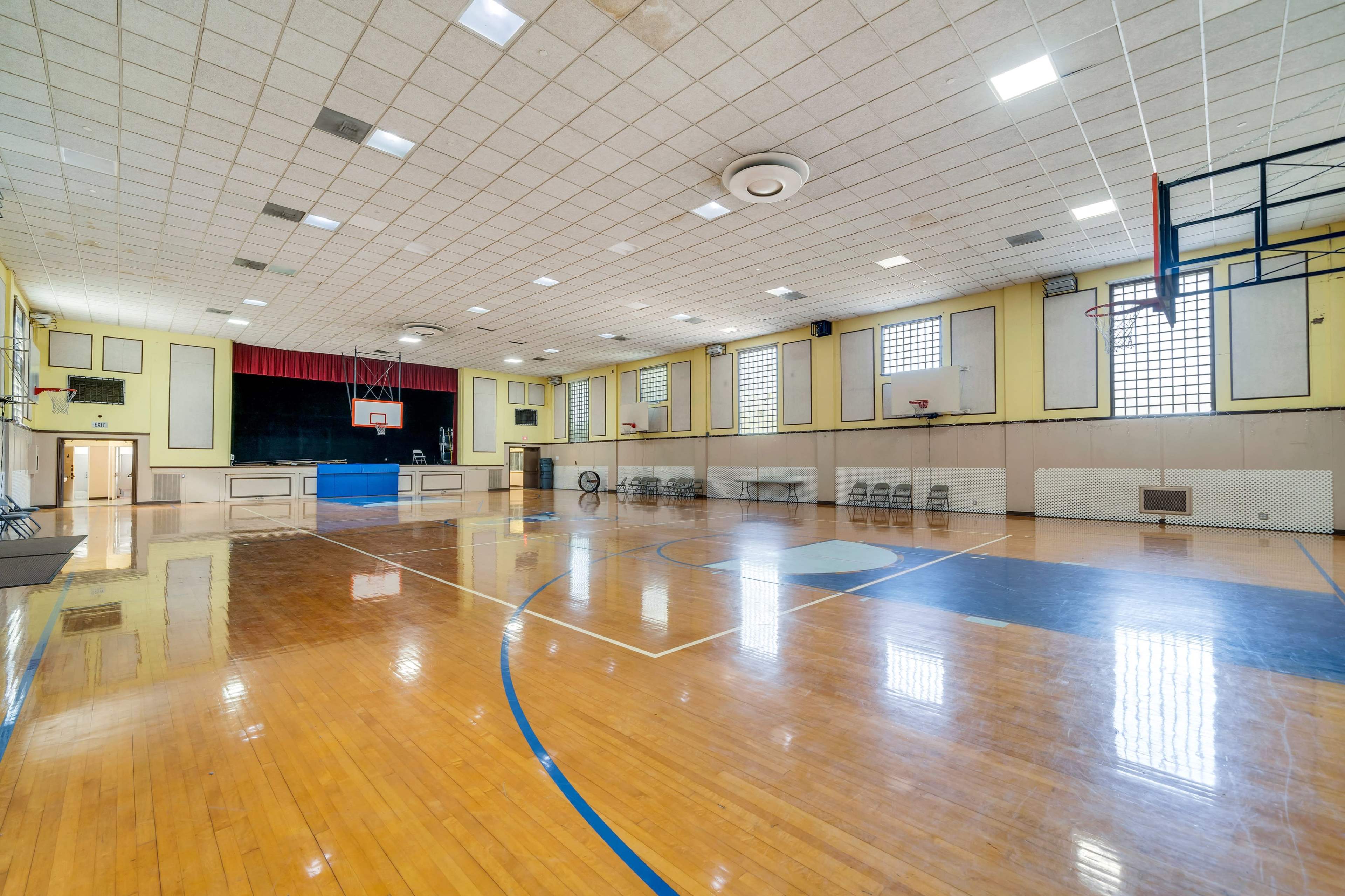 A spacious gymnasium with polished wooden floors, multiple basketball hoops, and several rows of folding chairs along one side.