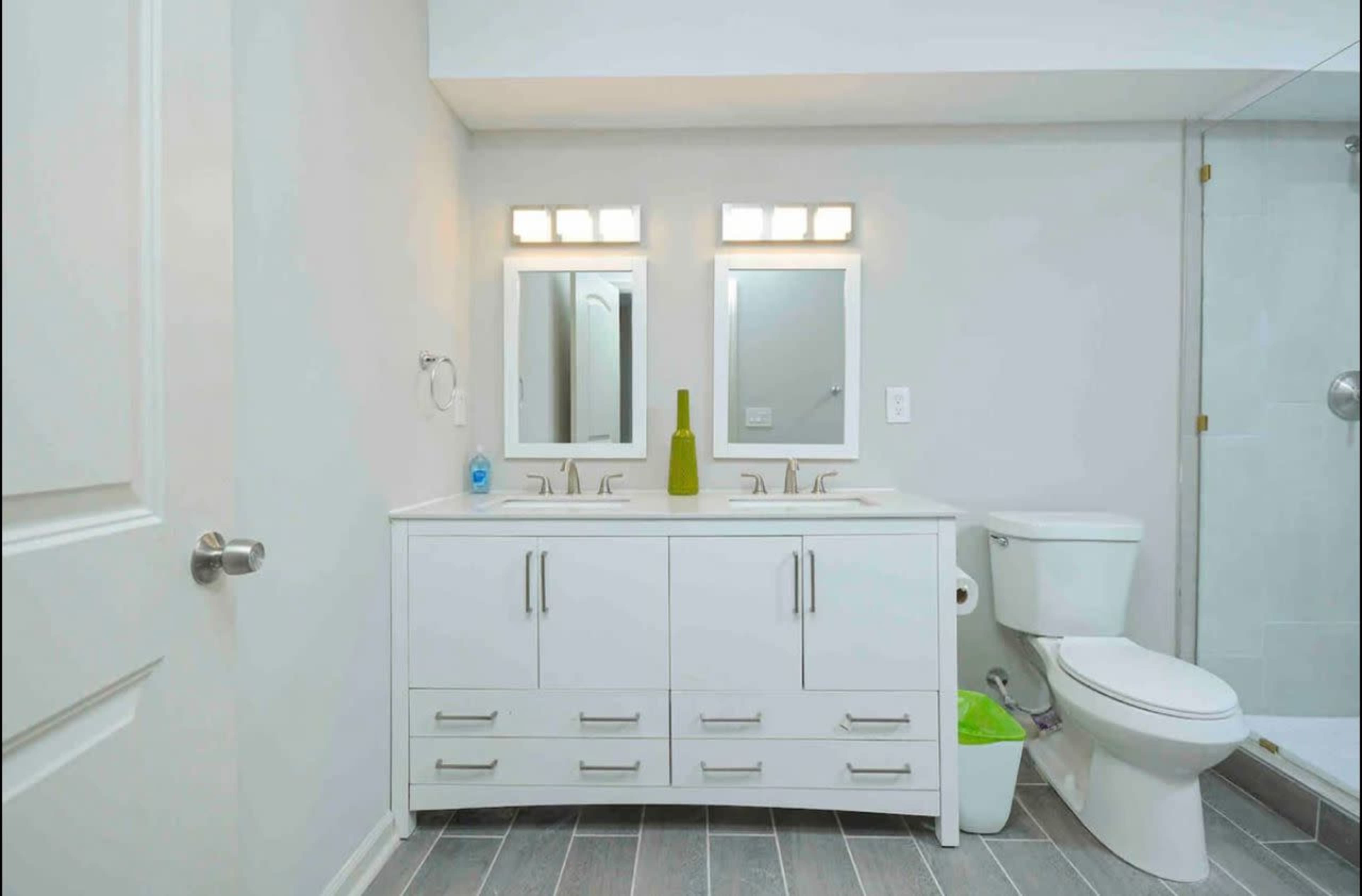 The bathroom features a double sink vanity with storage drawers, two mirrors, a toilet, and a glass shower enclosure.