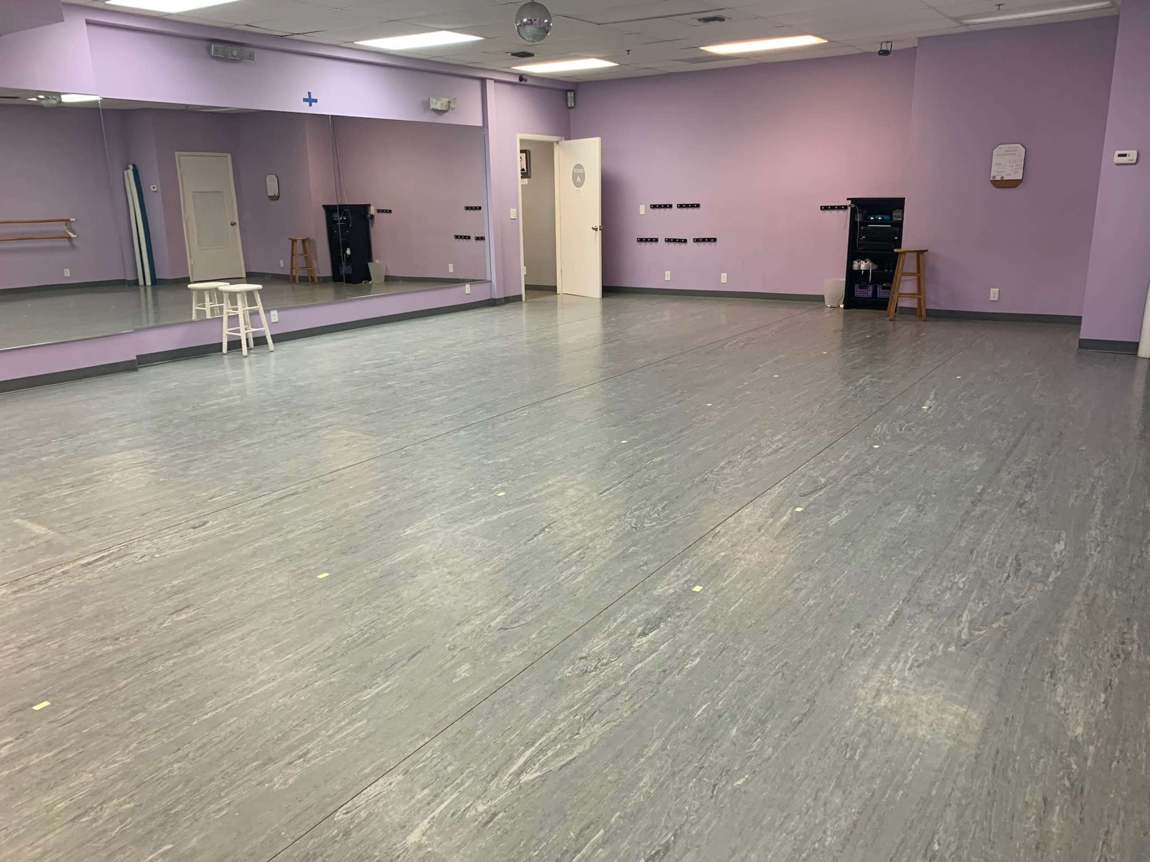 A dance studio with gray flooring, purple walls, and a mirrored wall on one side.
