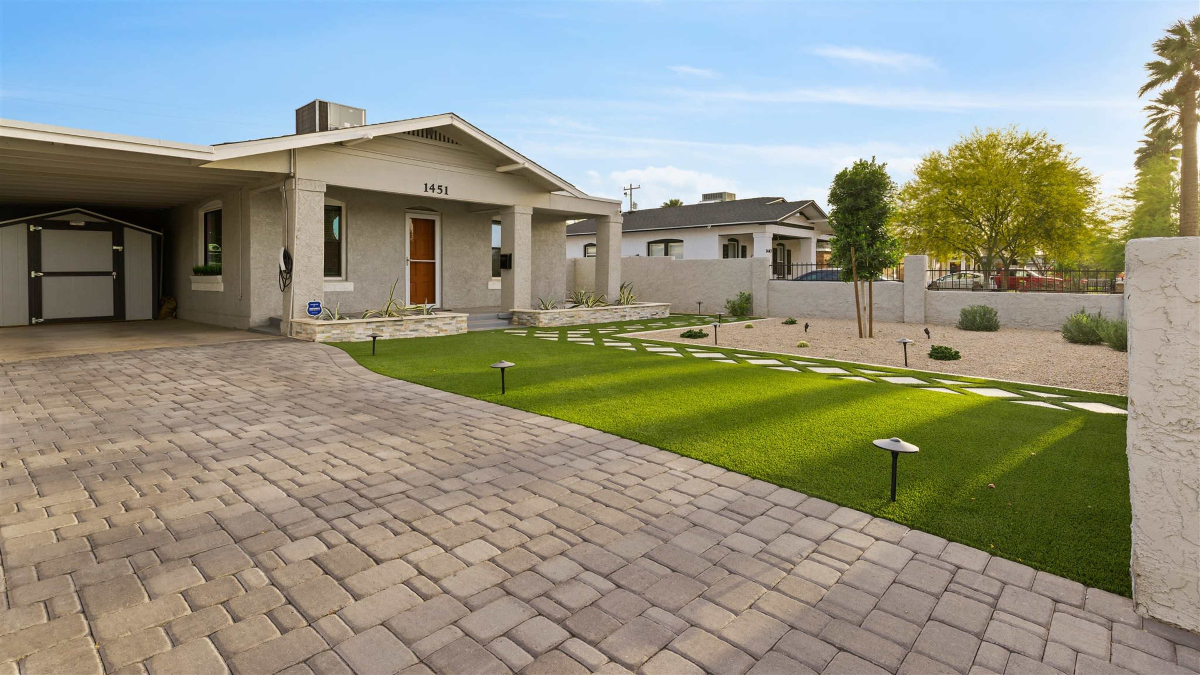 A modern house with a paved driveway features a landscaped front yard with artificial grass and a gravel area.