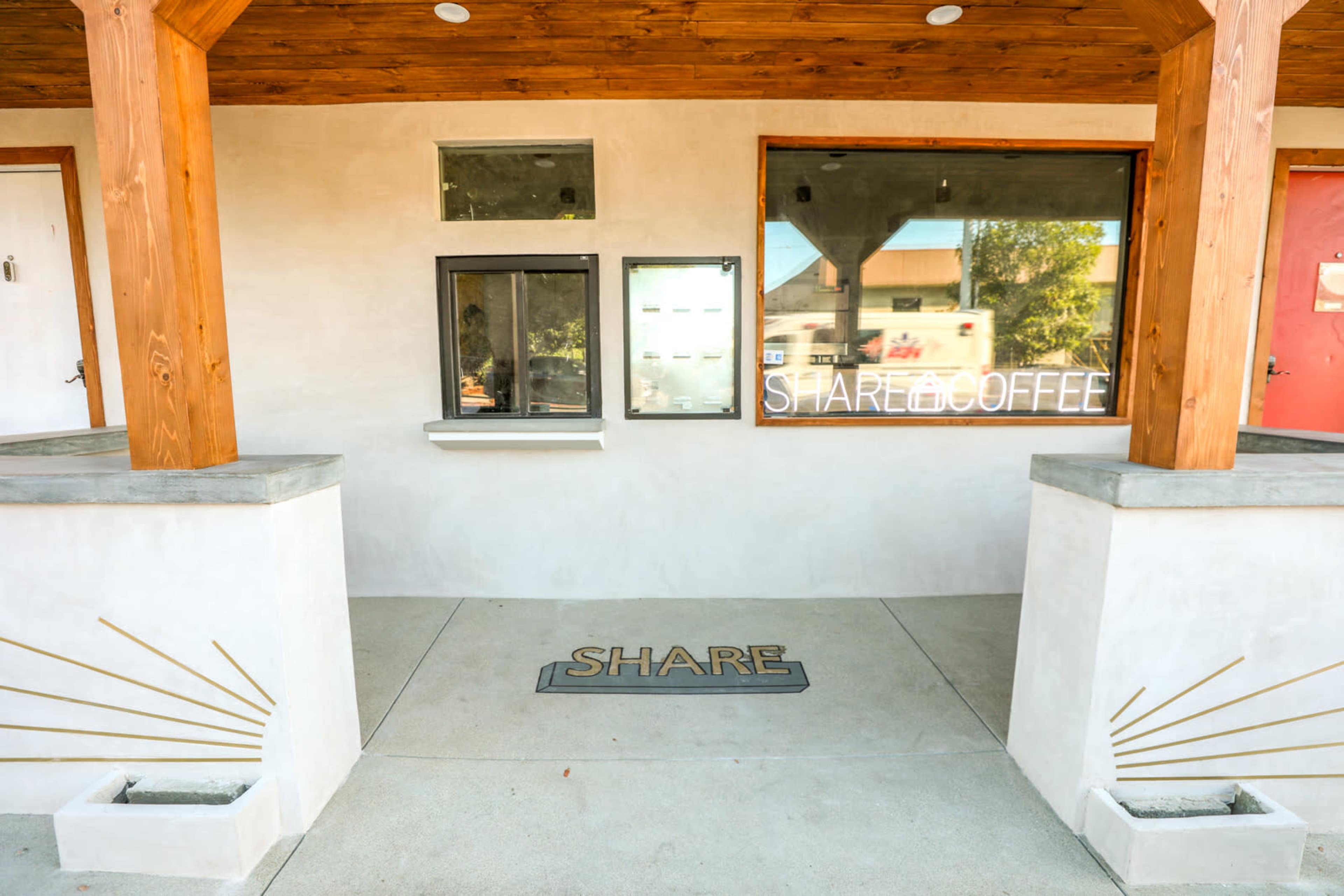 The exterior of a coffee shop with a serving window, a menu board, and a concrete pathway marked with the word "SHARE."
