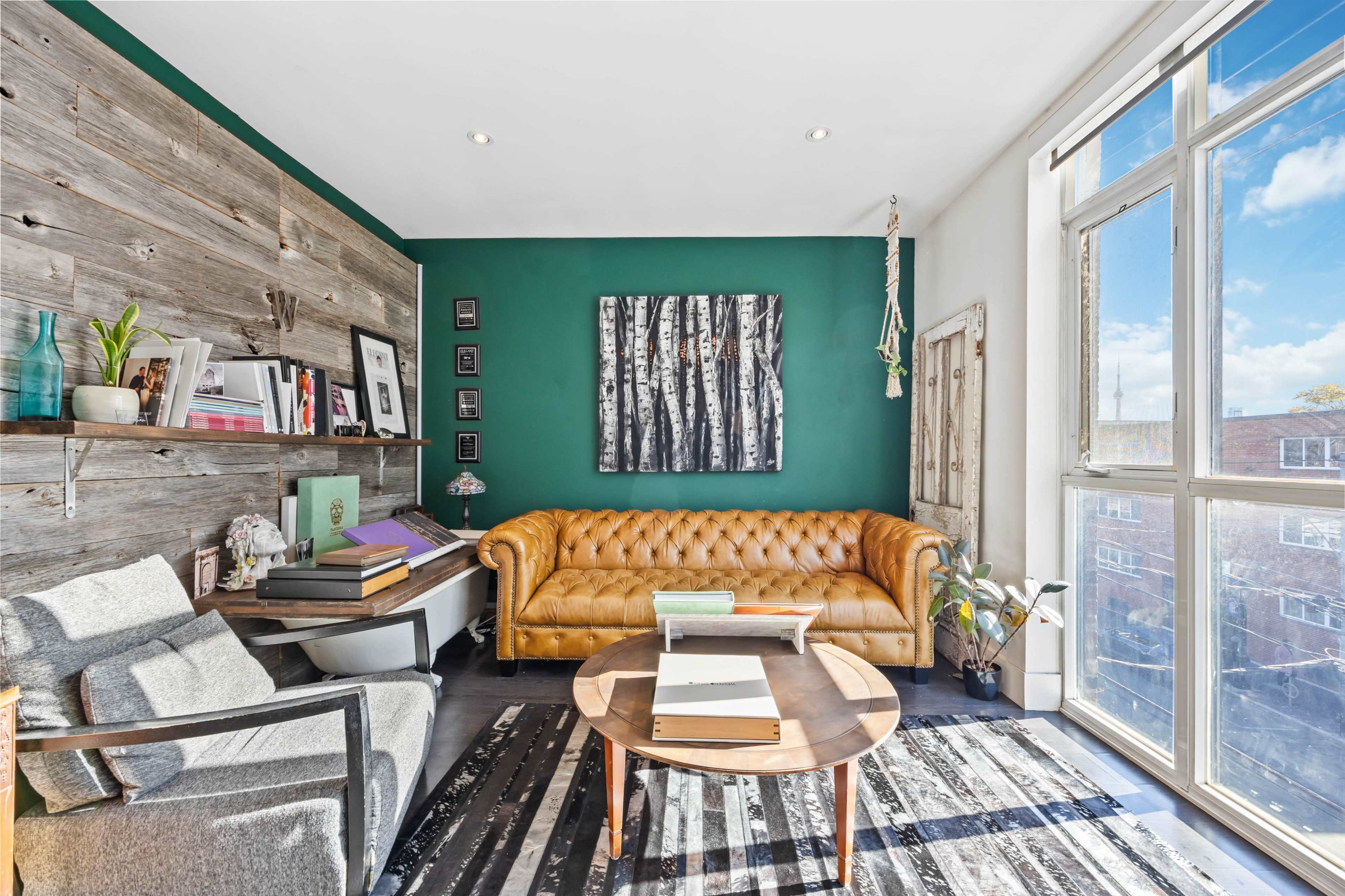A cozy living room features a brown leather couch, a round coffee table, and a mix of art and plants against a green wall.