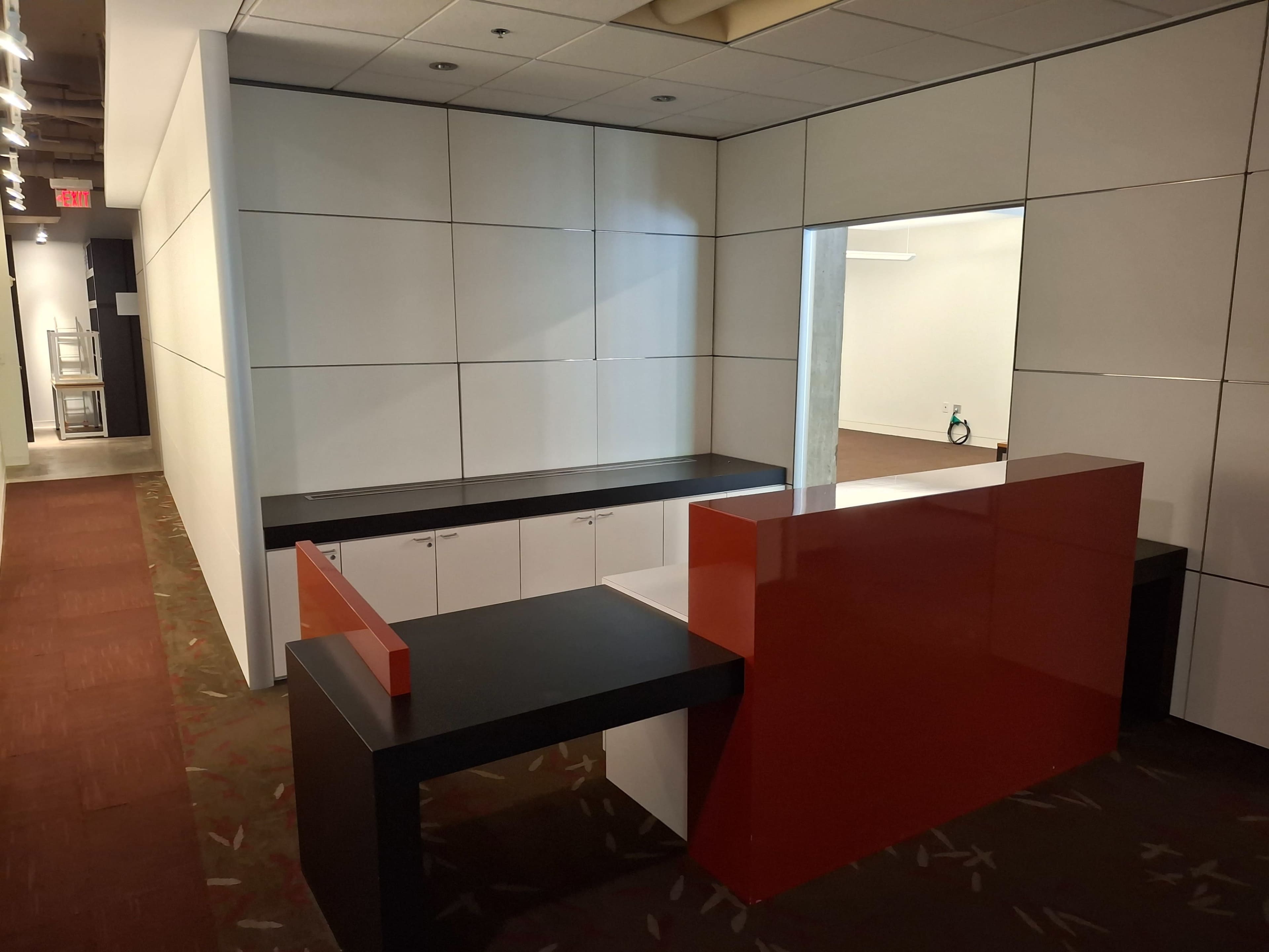 The image shows a modern reception area with a black and red desk next to a white wall, leading into an empty room.