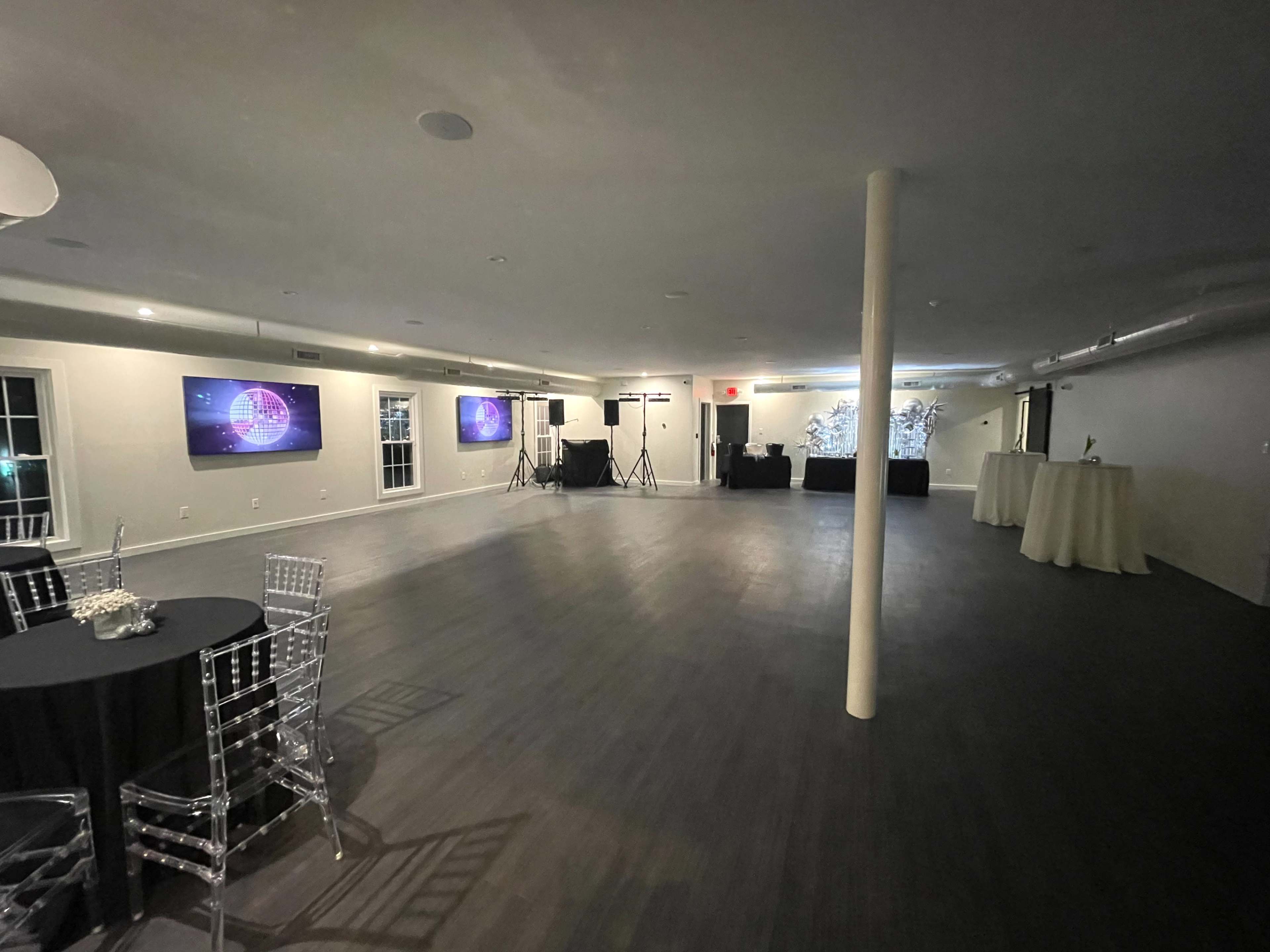 The image shows an empty event space with black tables set for guests and audiovisual equipment set up at one end.