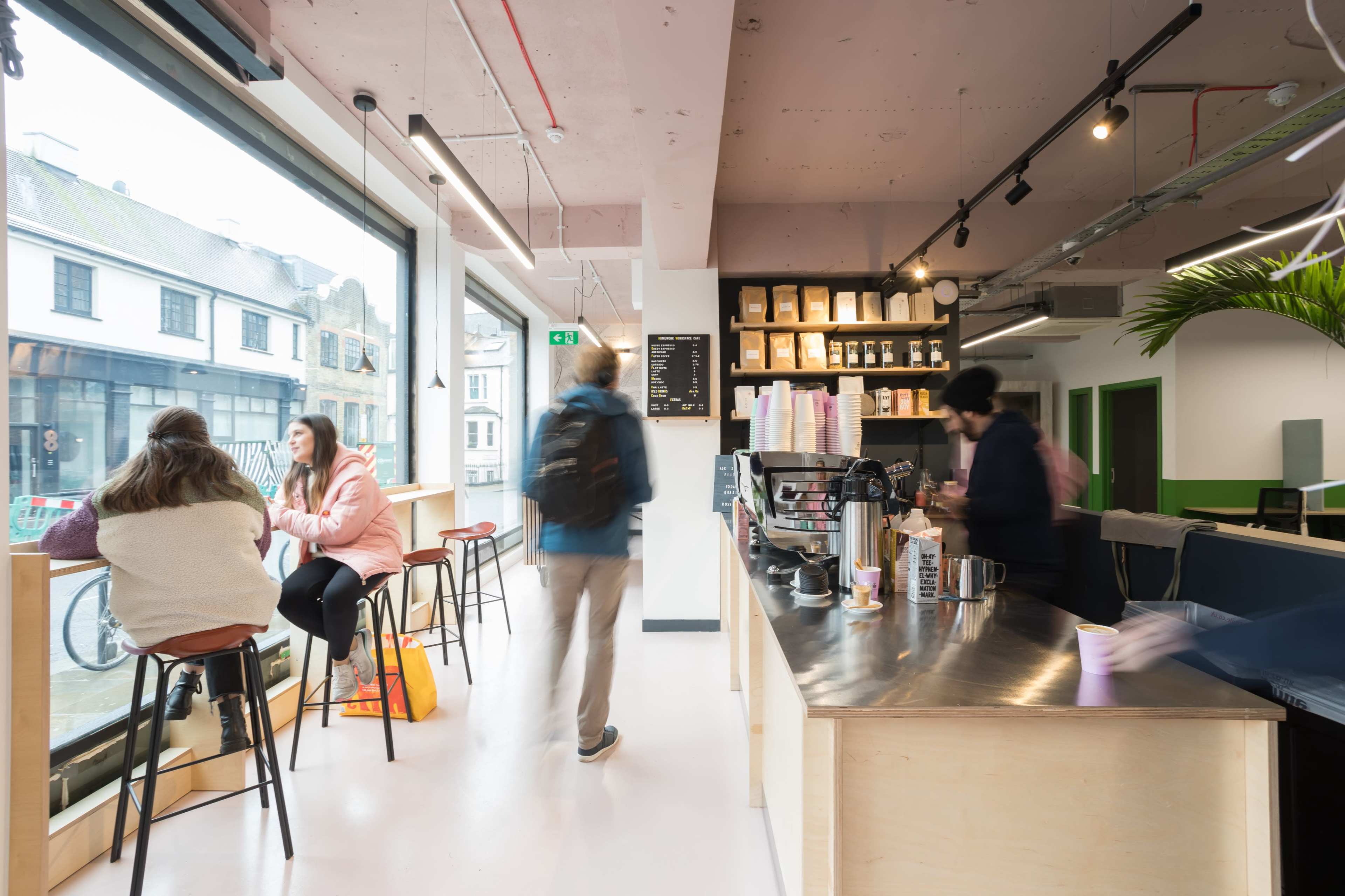 A café interior features customers sitting by large windows and a barista preparing drinks behind a counter.