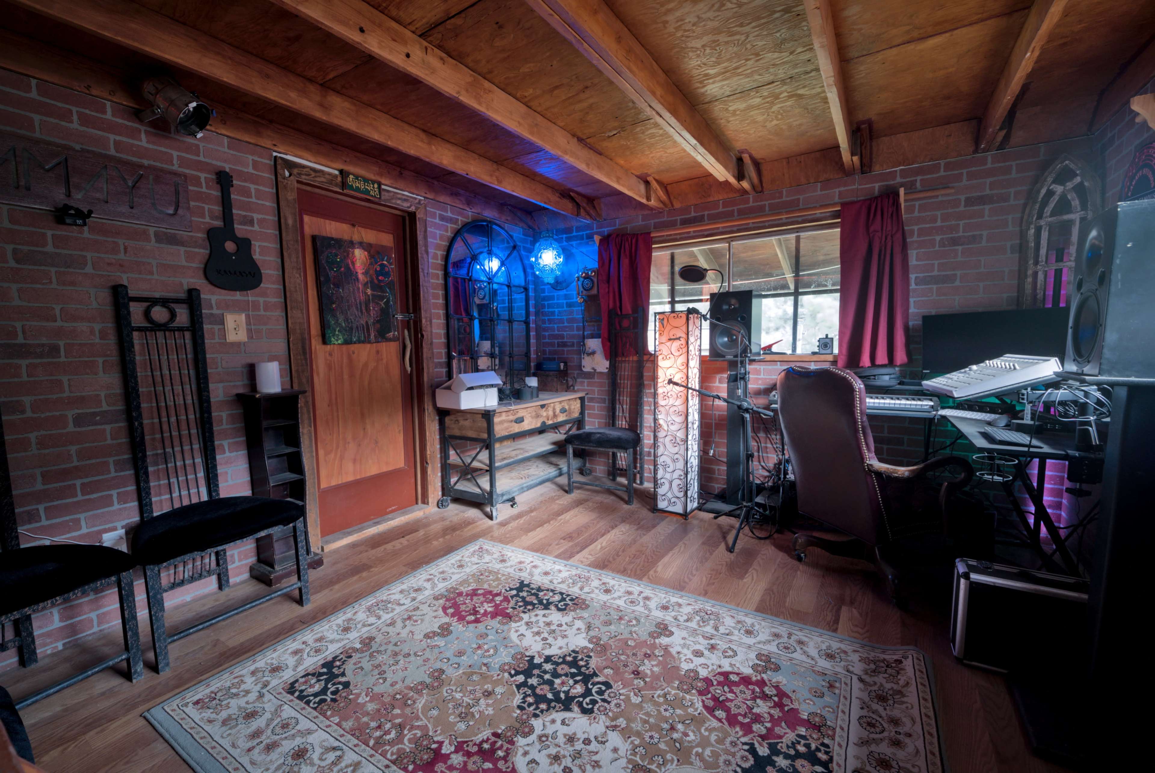 The image depicts a cozy music studio with brick walls, wooden beams, and equipment arranged around a workstation.