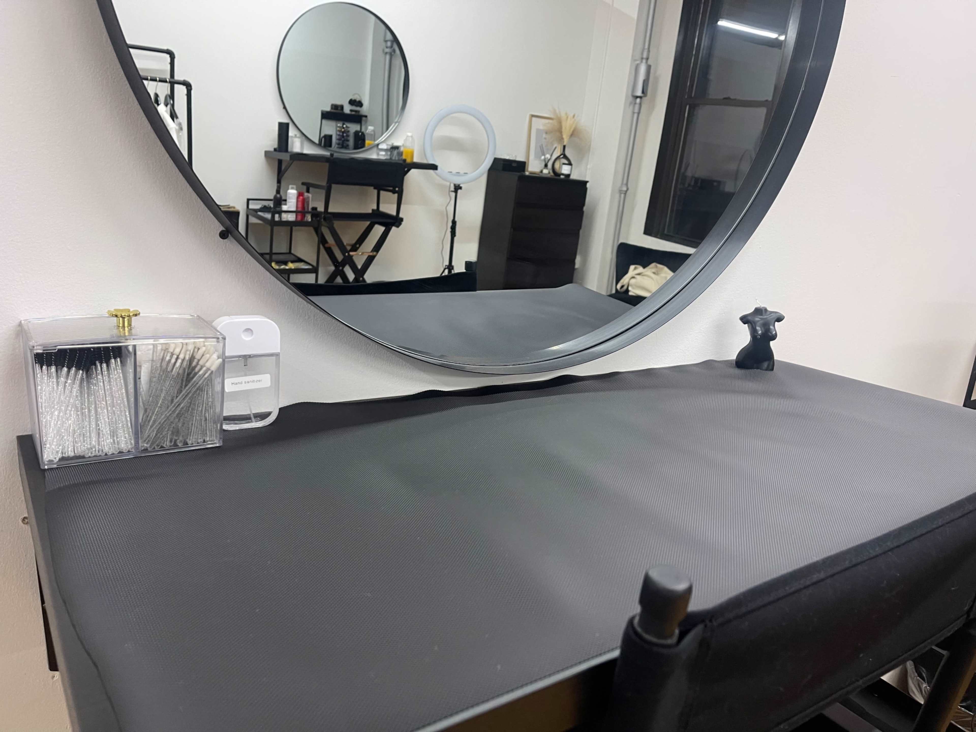 A black-topped vanity table is set against a wall, featuring a round mirror and a small collection of beauty tools.
