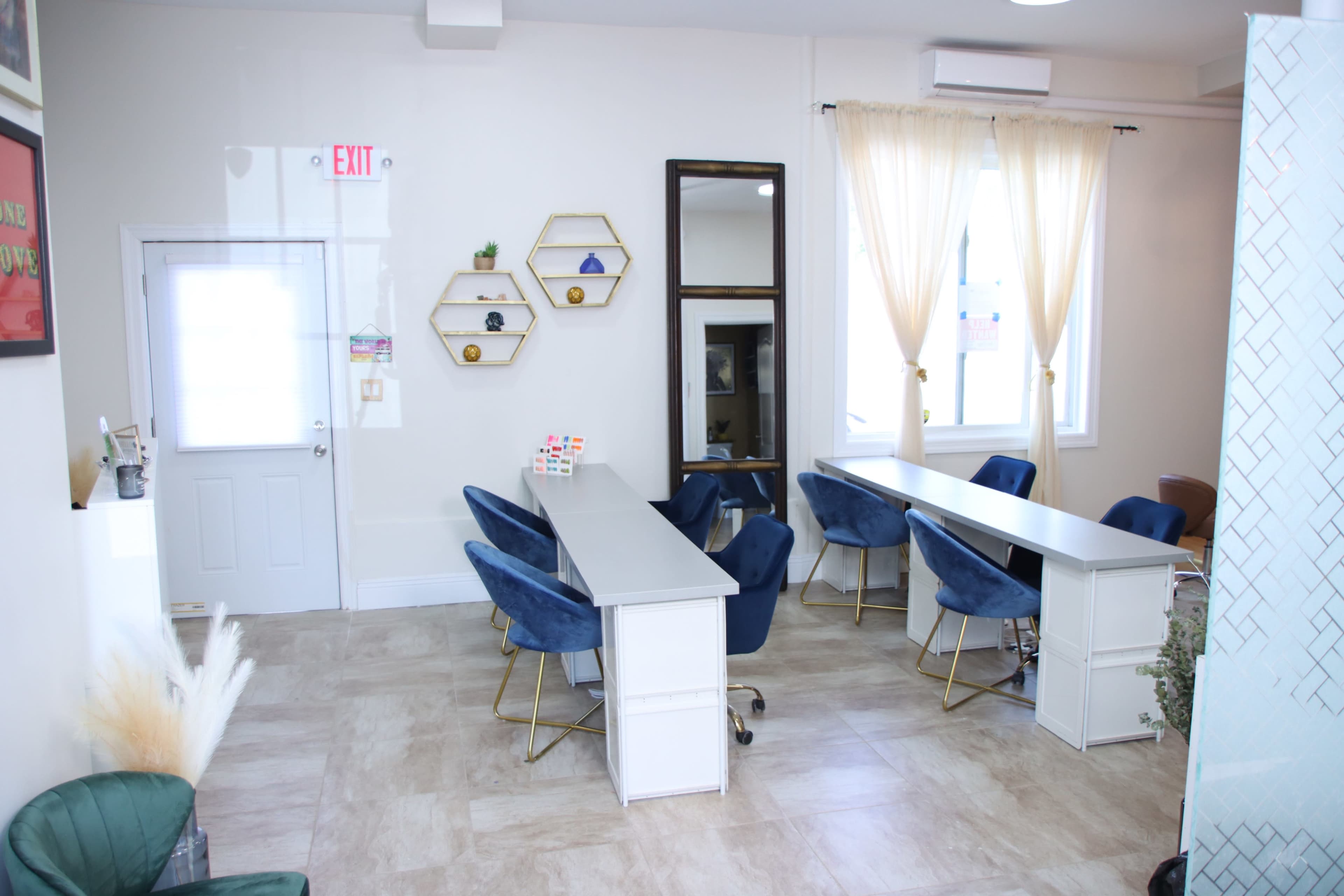 A modern interior workspace featuring several desks with blue chairs, decorative shelves, and large windows for natural light.