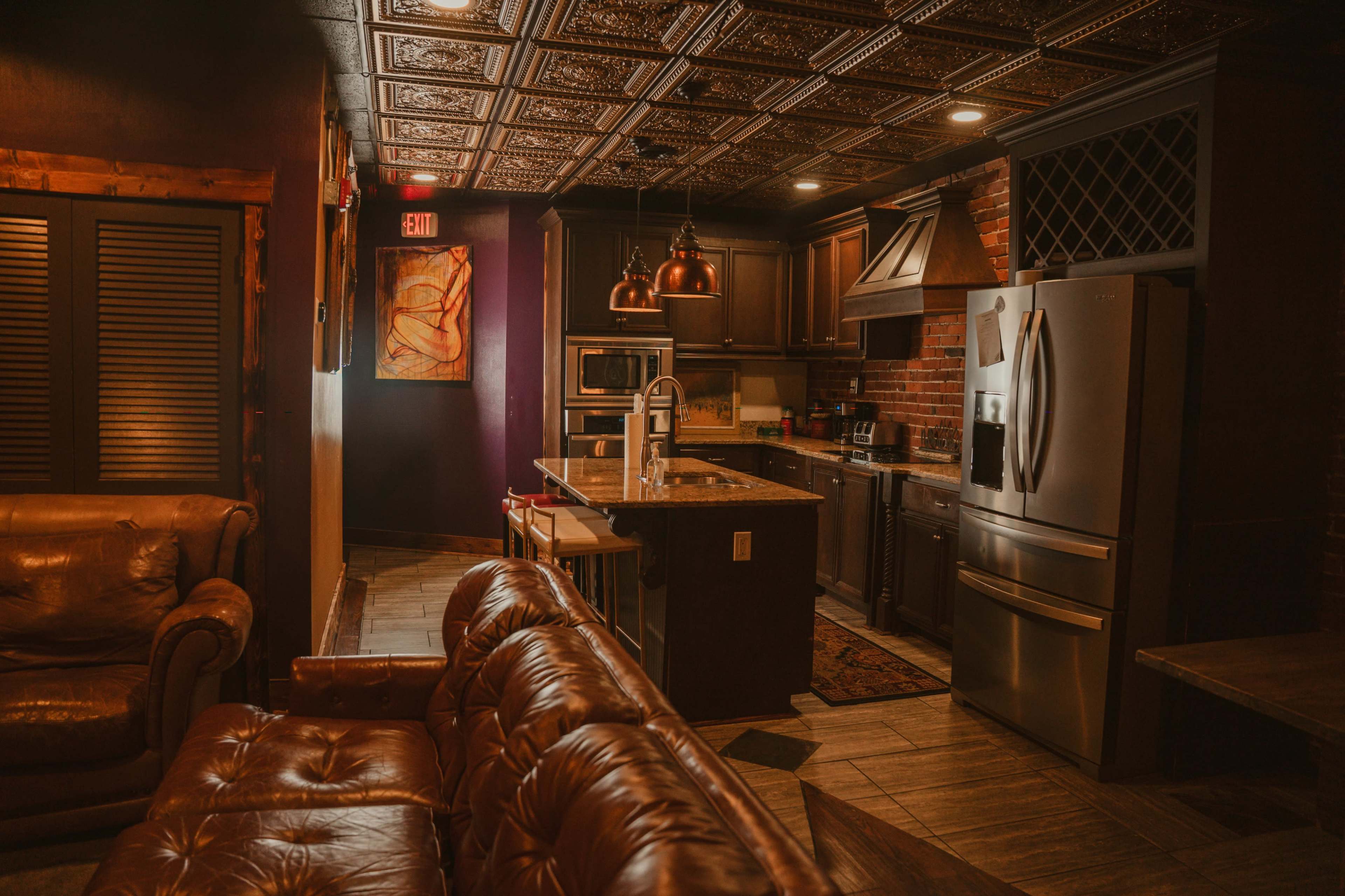 The image shows a modern kitchen with dark cabinetry and stainless steel appliances, adjacent to a cozy seating area featuring a leather sofa.