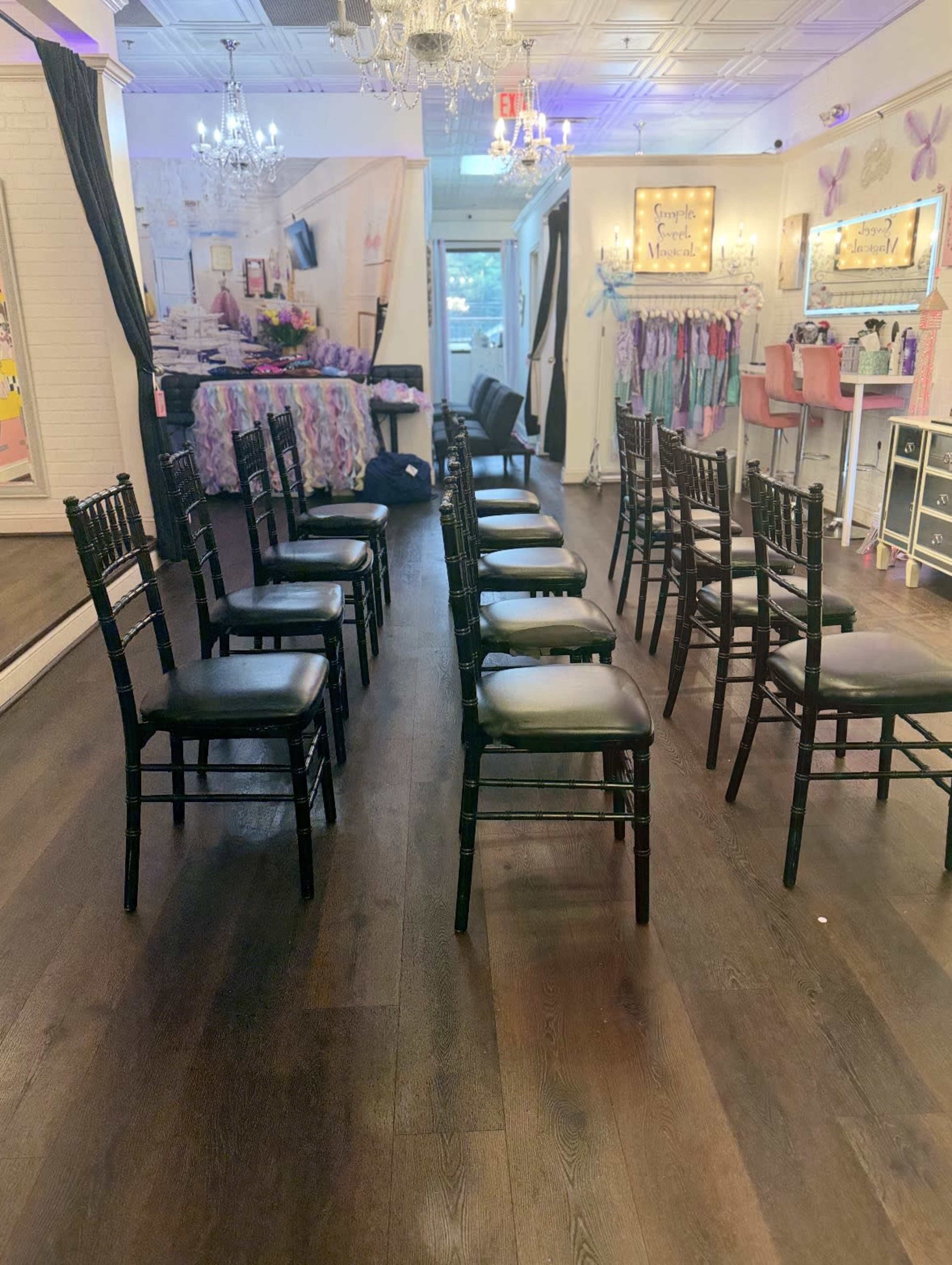 The image shows a row of black chairs arranged in a well-lit room decorated with colorful fabrics and mirrored walls.
