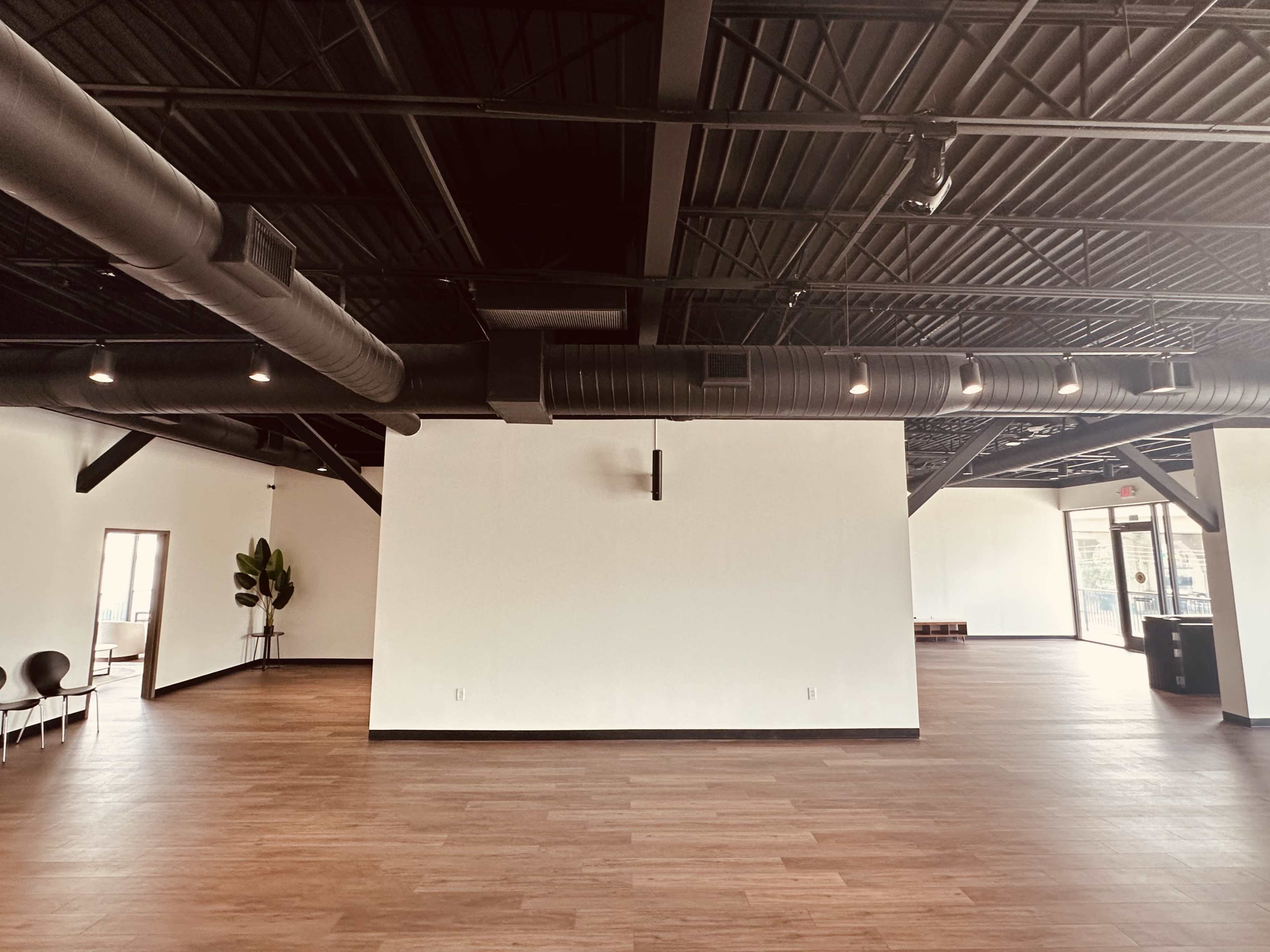A spacious, empty room with dark beams and ductwork on the ceiling, wooden flooring, and large walls ready for decoration.